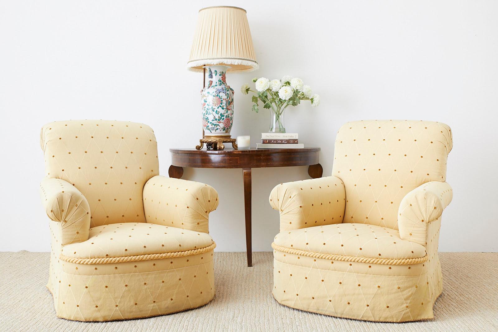 Bespoke pair of oversized club chairs featuring English style rolled arms and a scrolled back. Upholstered in a light citron yellow fabric with a geometric diamond pattern design and round chenille accents throughout. The fronts have a decorative