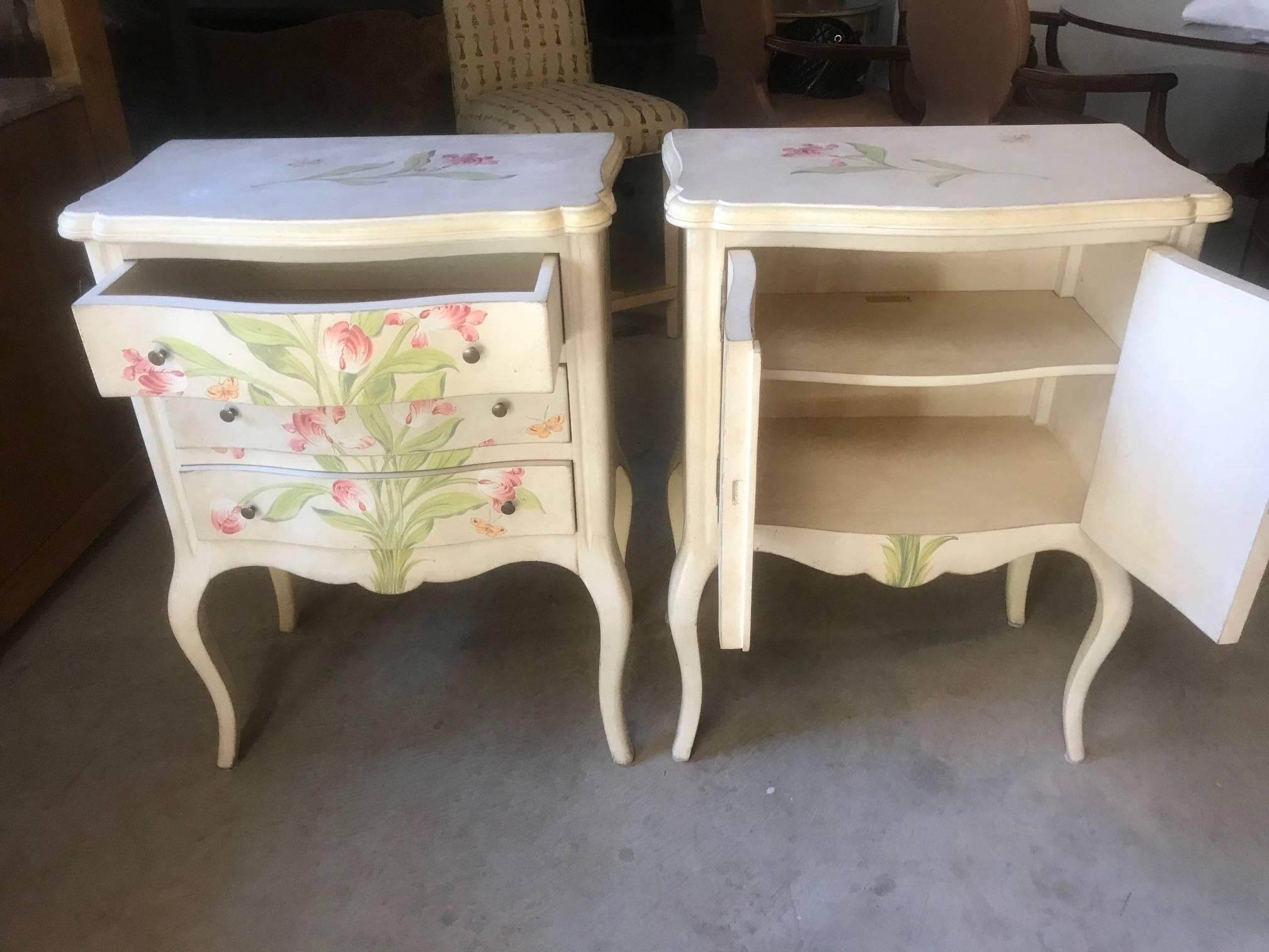 Paire de tables de nuit haut de gamme peintes à la main, l'une est une petite commode, tandis que l'autre est un meuble à deux portes. Le fond est un blanc cassé vieilli et les fleurs et papillons sont des nuances de rose, de vert et d'or jaunâtre