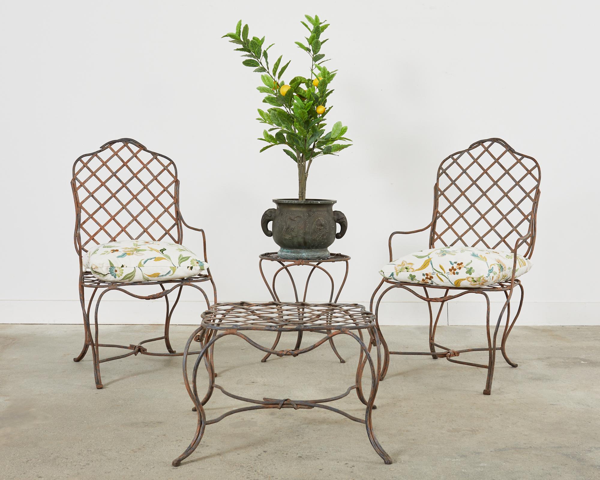 Distinctive pair of wrought iron dining armchairs with matching ottoman made in the neoclassical style and manner of Rose Tarlow or Gregorius Pineo. Hand-crafted by a foundry in Los Angeles, CA with geometric lattice inset seat and back. The thick