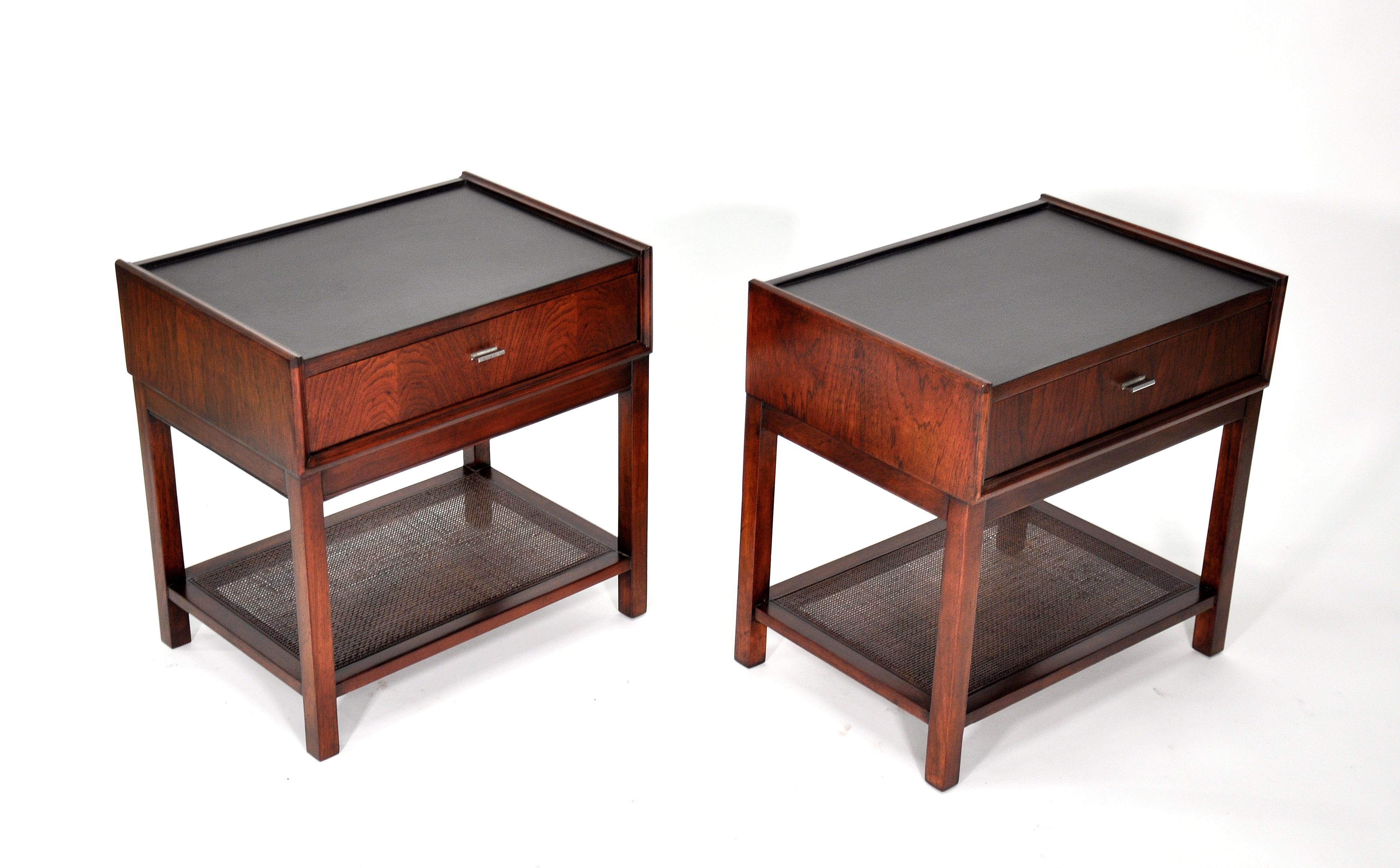 A gorgeous pair of vintage Mid-Century Modern two-tier rosewood side or end tables manufactured by Founders Furniture in the 1960s, often attributed to Harvey Probber. Two-tiered, fitted with a caned magazine shelf and a black leather top; the