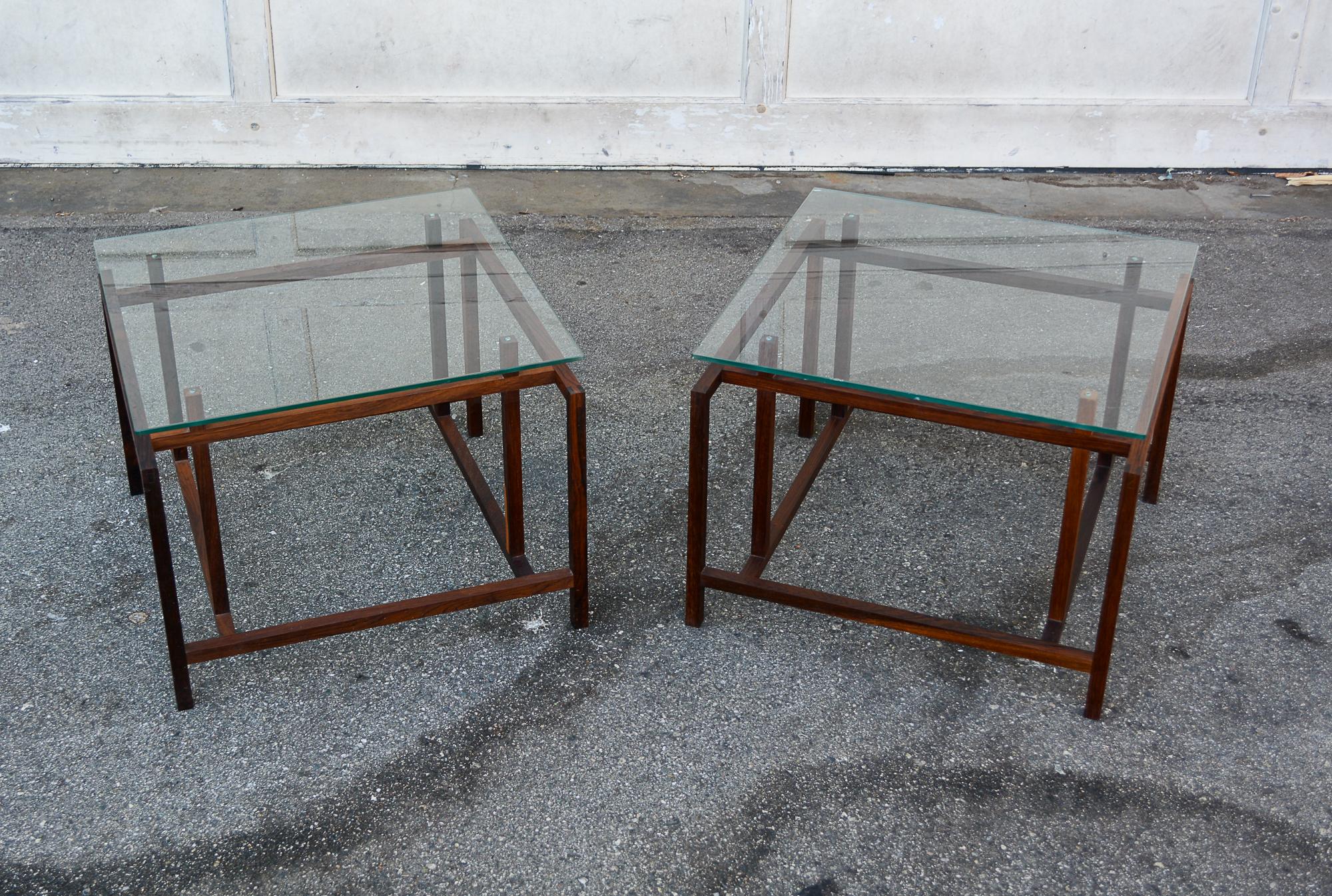 Pair of rosewood and glass end tables designed by Henning Norgaard. The frames are solid Brazilian rosewood. These are in original condition. The glass top on one table has a few small chips to the edges. There is a small crack in one wood piece.