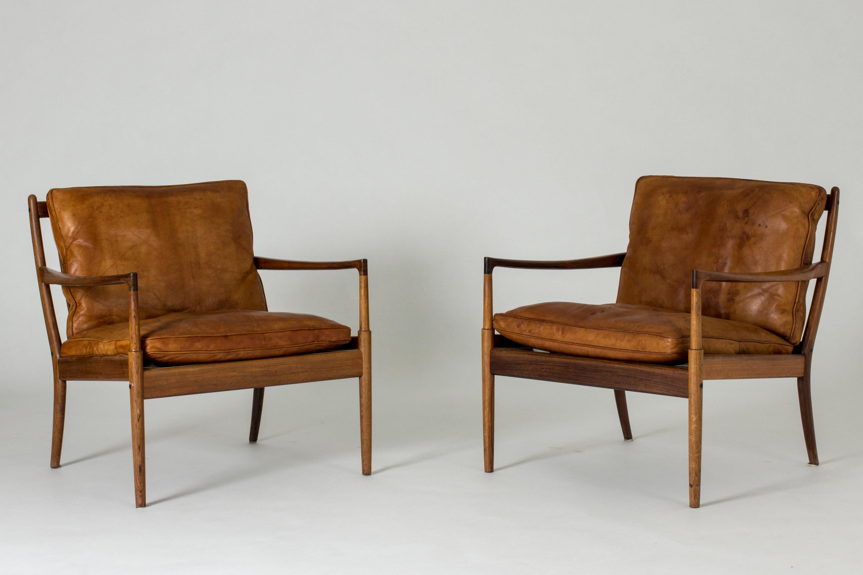 Pair of beautiful “Samsö” lounge chairs by Ib Kofod Larsen, made from rosewood with loose leather backs and seats. Stunning slender armrests in a sculpted design.