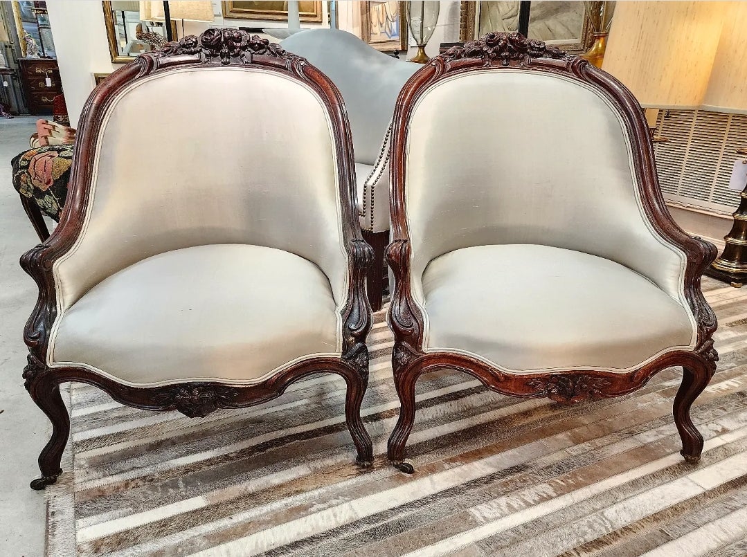 An exceptional pair of French Rococo Revival slipper chairs in Rosewood. Each chair meticulously carved with intricate detailing of flora-form in various states of bloom. Retaining the original wooden rollers and brass casters. These have been