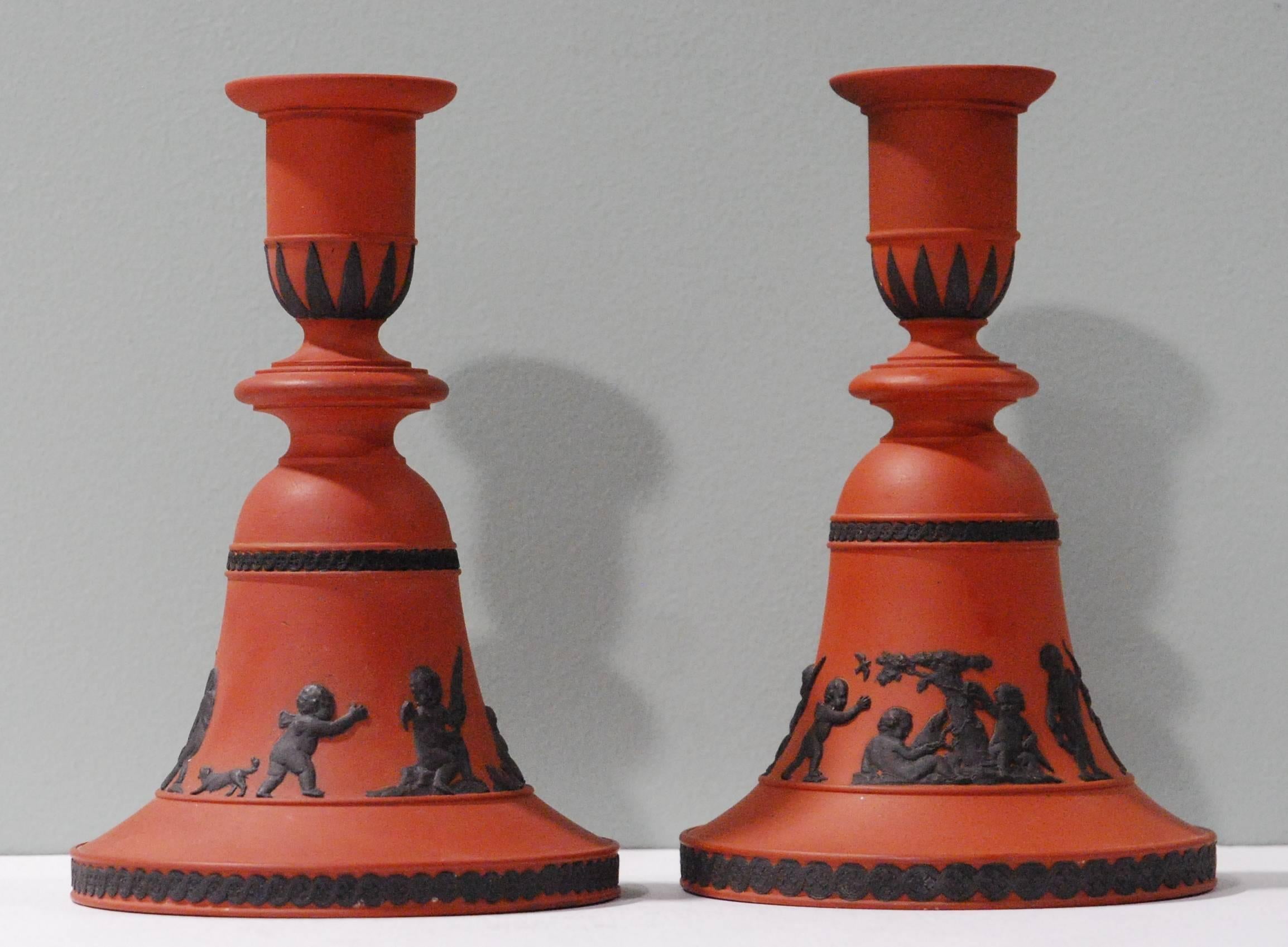 A rare pair of bell shaped candlesticks in rosso antico, with black decoration of ‘Boys at Play’.