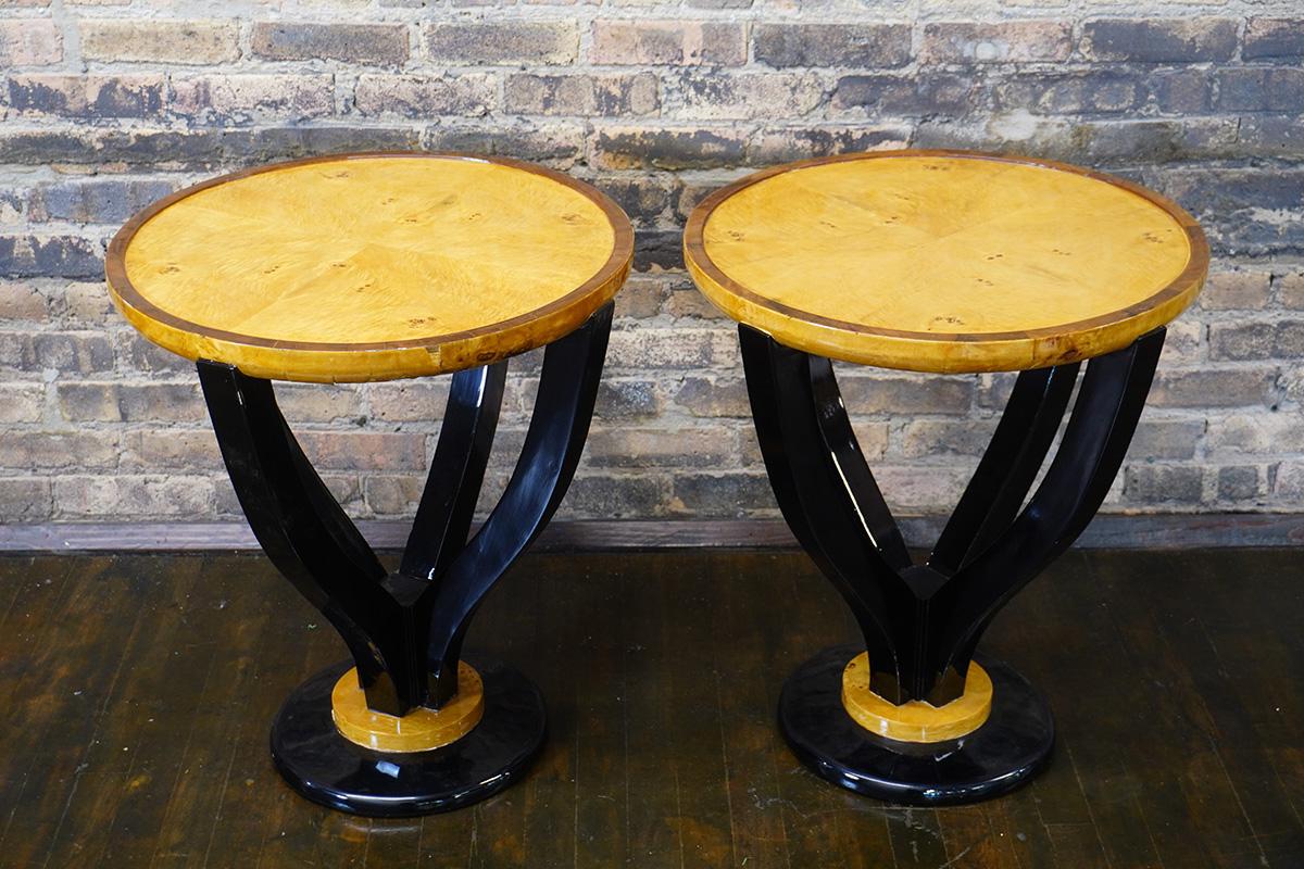 Pair of Art Deco style round end/side tables.  They feature a small footprint at the base (largely ebonized).  There are four ebonized supports to a round burl wood table top that has a walnut trim at the outer edge.  

The finish is high gloss