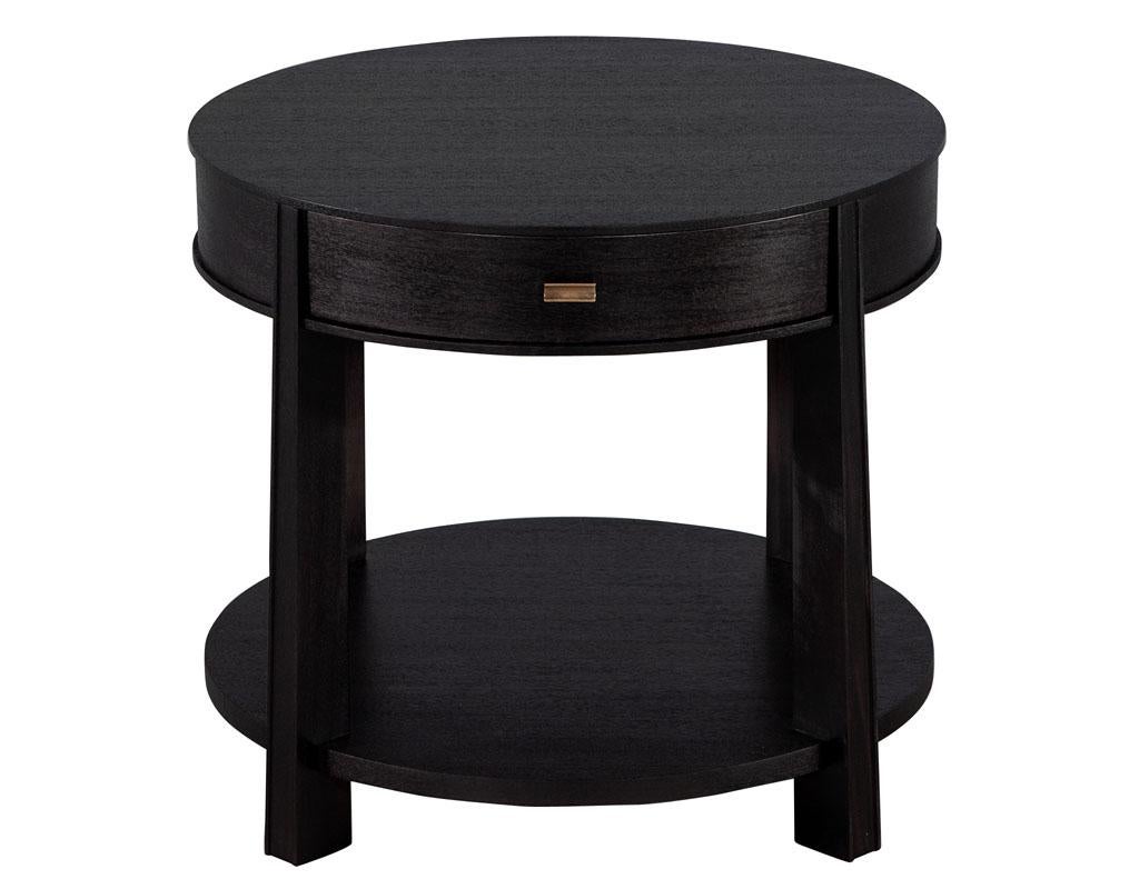 Pair of round black nightstand side tables by Barbara Barry Baker Furniture. Round mahogany tables with single storage drawer and open shelf design. Finished in a textured satin black lacquer. Completed with brass handle and felted interior drawer.