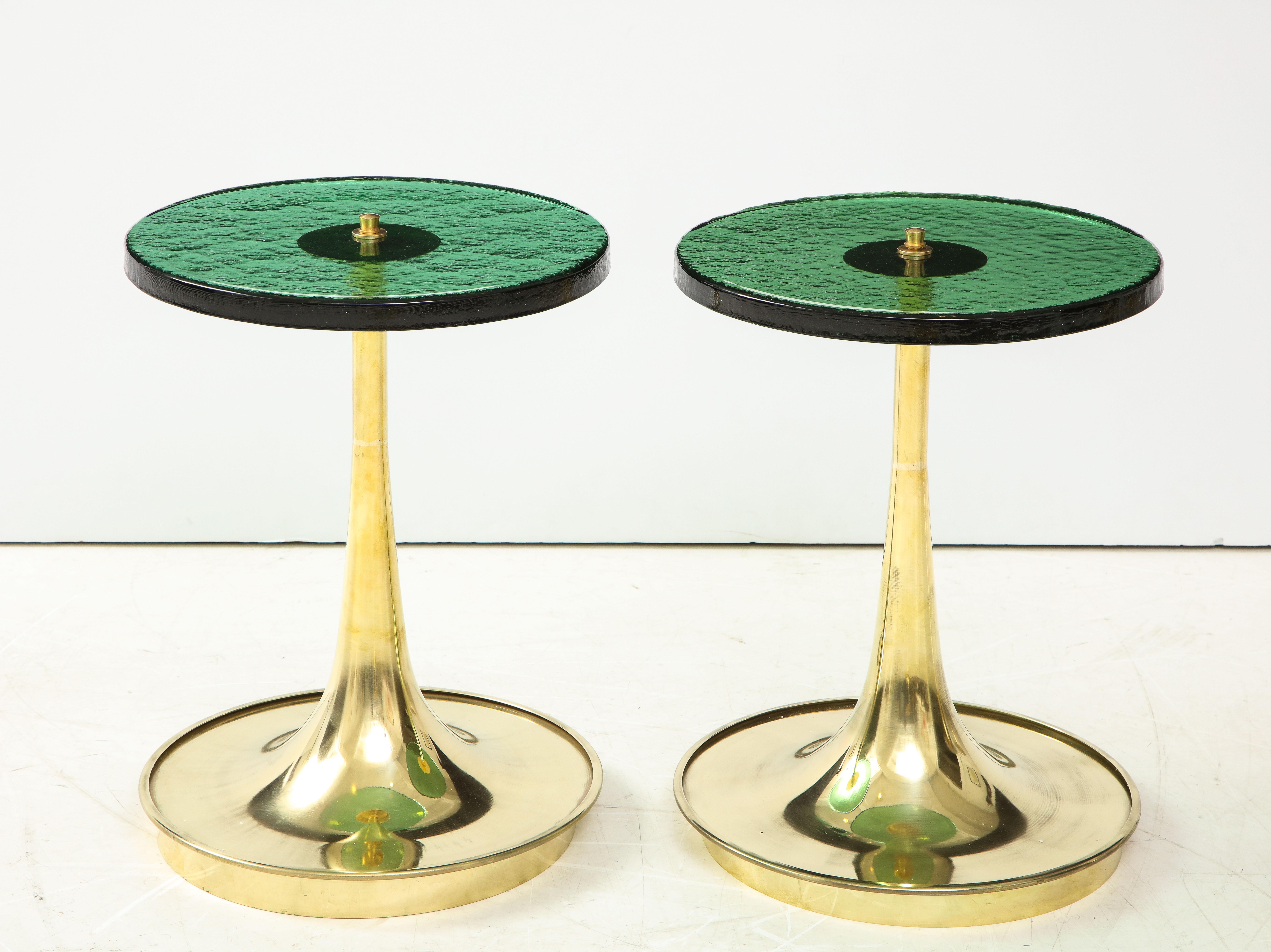 Pair of round emerald green murano glass top and brass martini tables, Italy. Hand-casted thick and solid emerald green Murano round glass sits atop a hand-turned trumpet-shaped brass base. Modern flat top brass finial screws the glass top to the