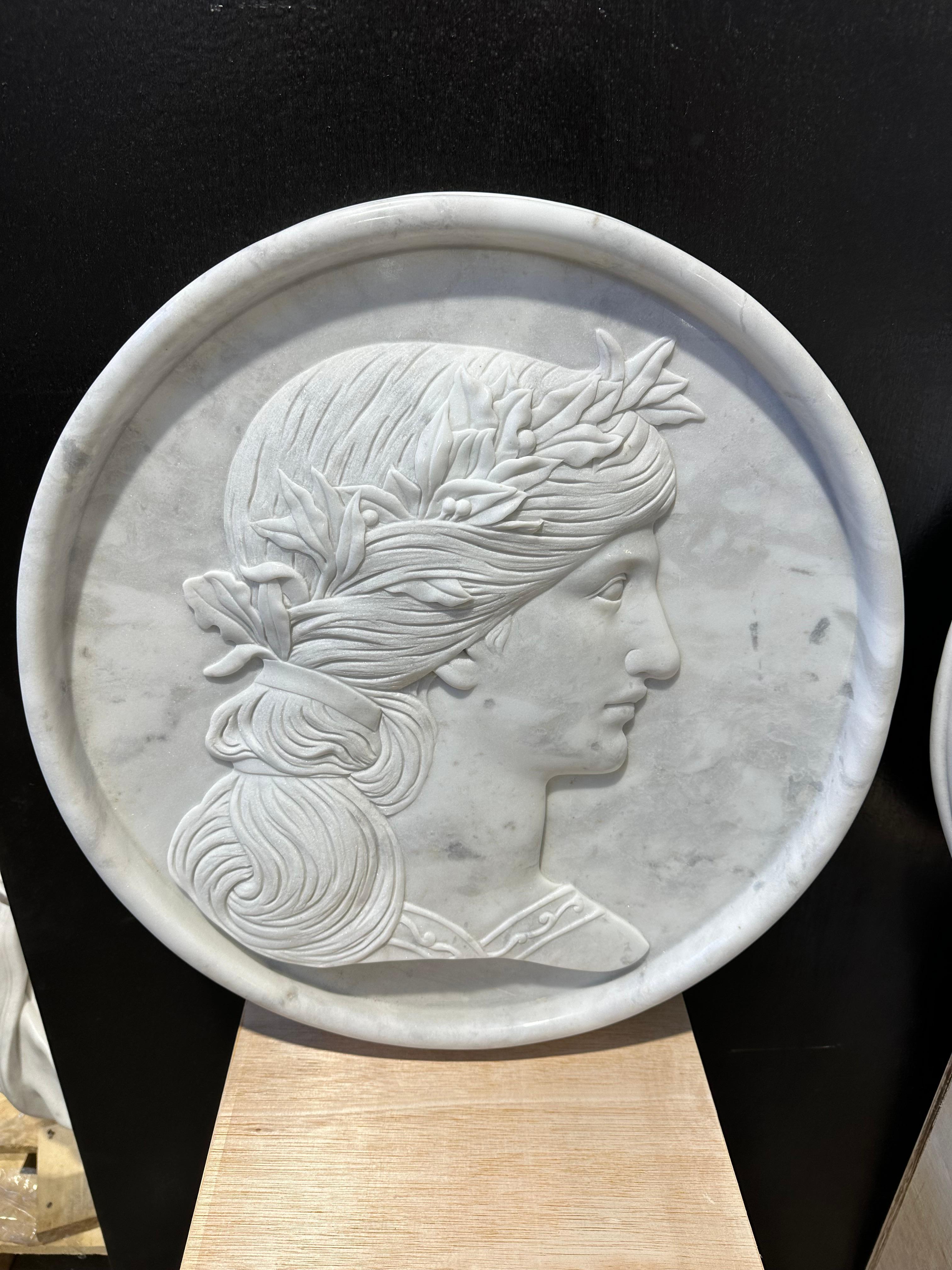 A very attractive pair of round marble wall plaques, depicting two female figures in side profile. The features are crisply carved and clear with detailing to the braided hair which is wound around floral wreaths and ribbons. A very decorative set