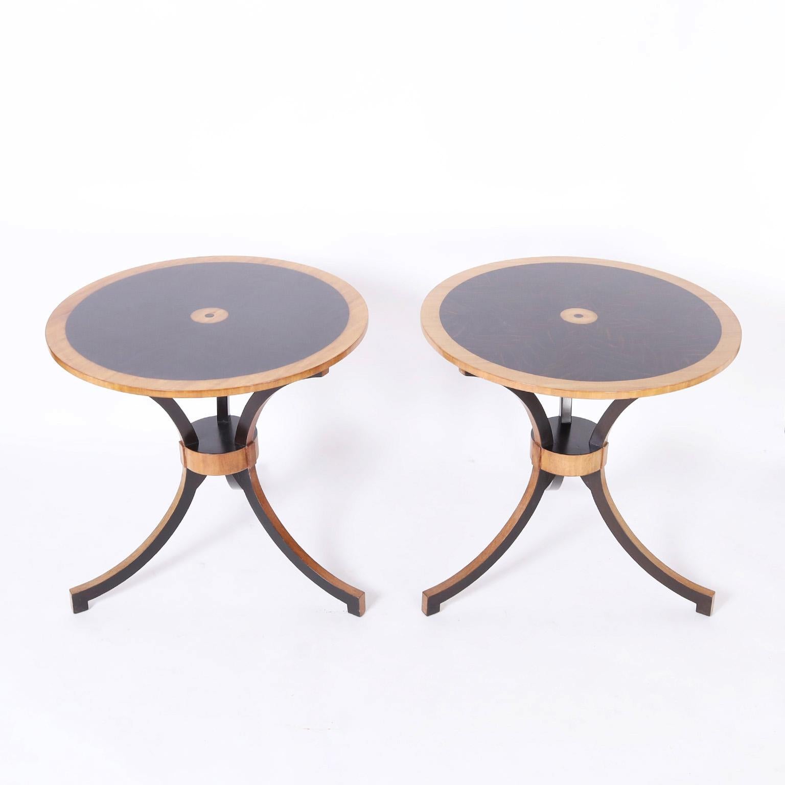 Dashing pair of midcentury tables crafted in bleached mahogany in a neoclassic form with a Biedermeier influenced pallet having round tops painted and decorated with a center medallion on a stylized hourglass form base.