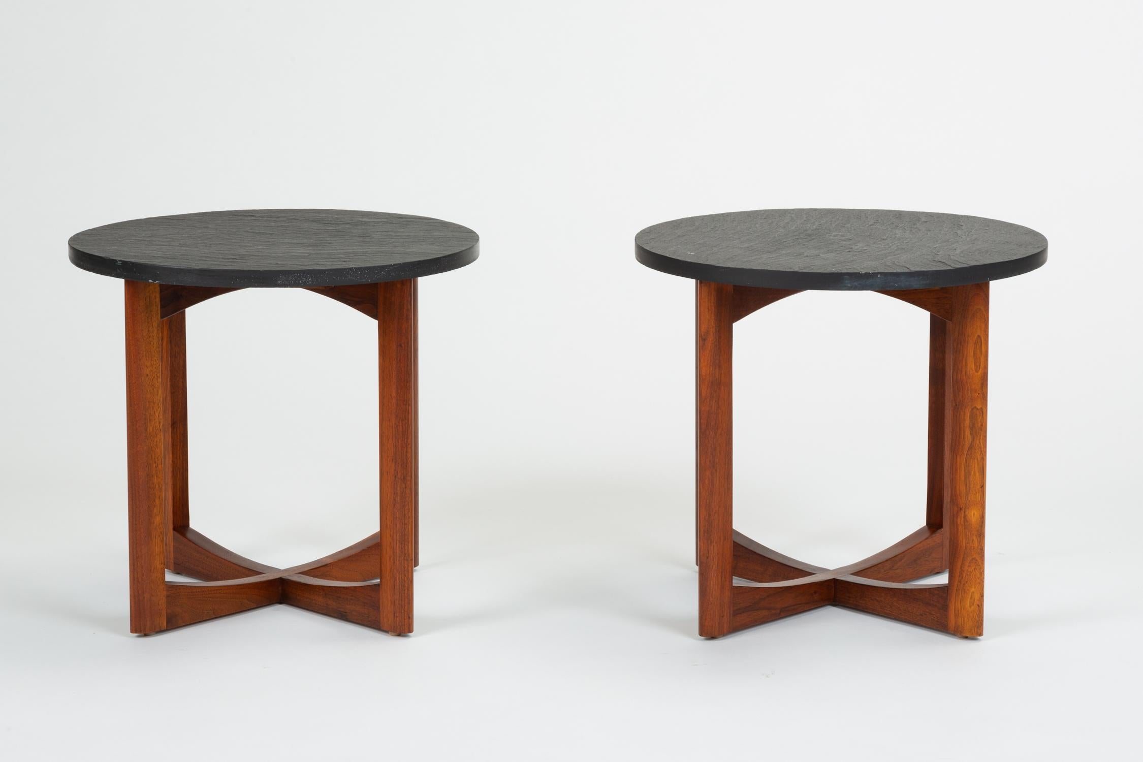 A pair of round, Mid-Century Modern side tables. Each table has a round top of textured slate sitting on four legs of solid, slightly tapered walnut. Solid walnut support beams sit on the ground in an X formation. Unsigned. 

Condition: Excellent