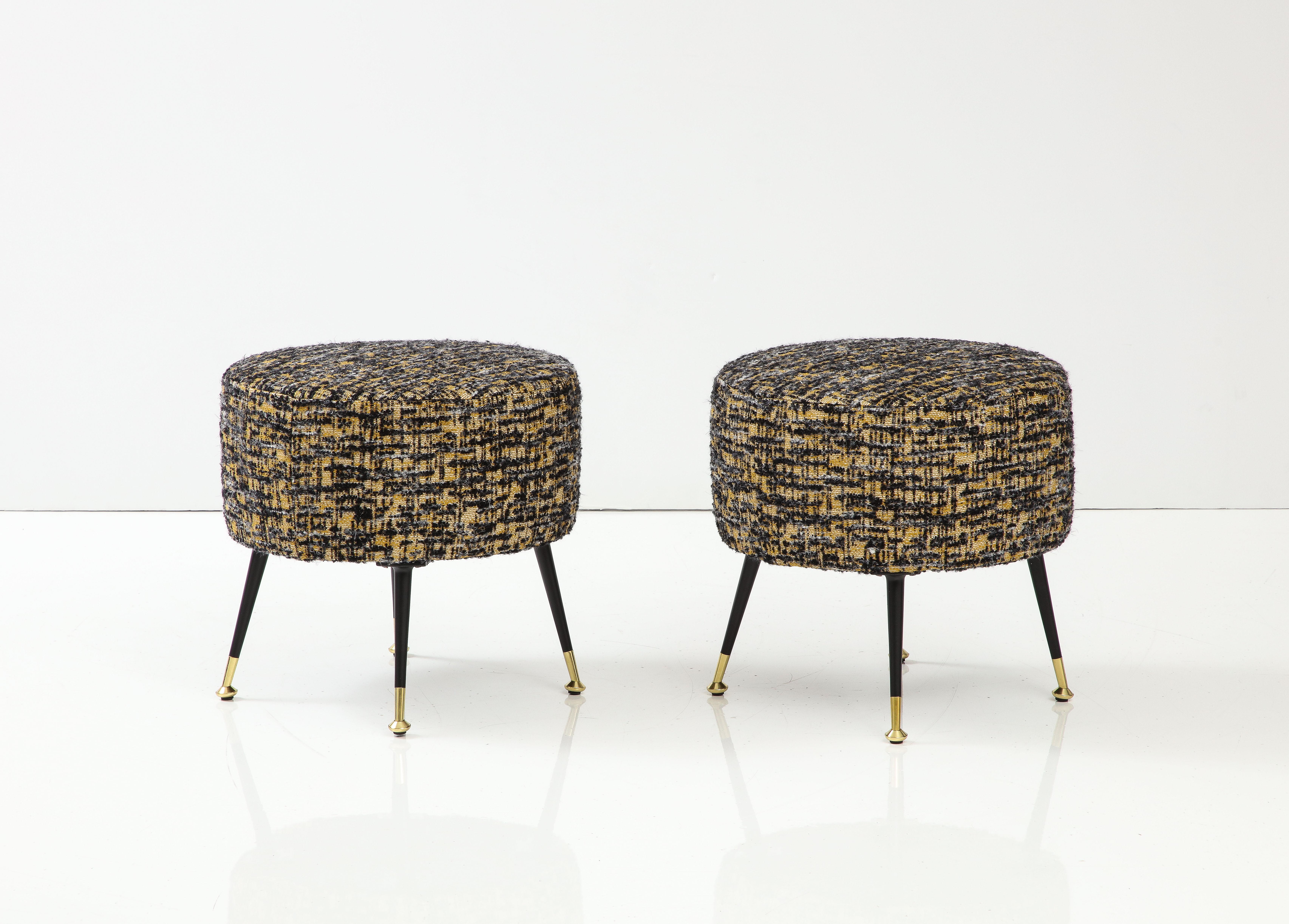 Pair of round stools or poufs handmade in Florence, Italy, by a master furniture artisan. Round seats upholstered in variegated boucle fabric by Dedar in black, muted yellow and ivory hues with lacquered black lacquered steel and brass legs. This