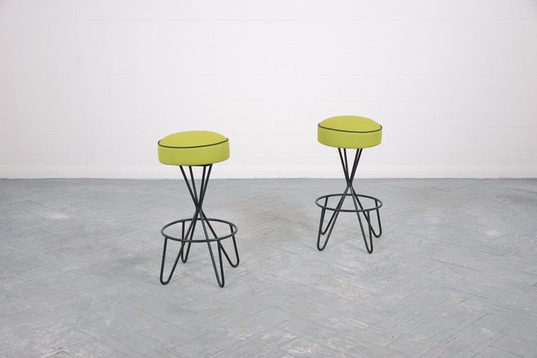 This extraordinary pair of mid-century modern swivel bar stools are in great condition beautifully crafted has a wrought iron base is newly painted in a black color finish and has been professionally restored by our expert craftsmen. The swivel