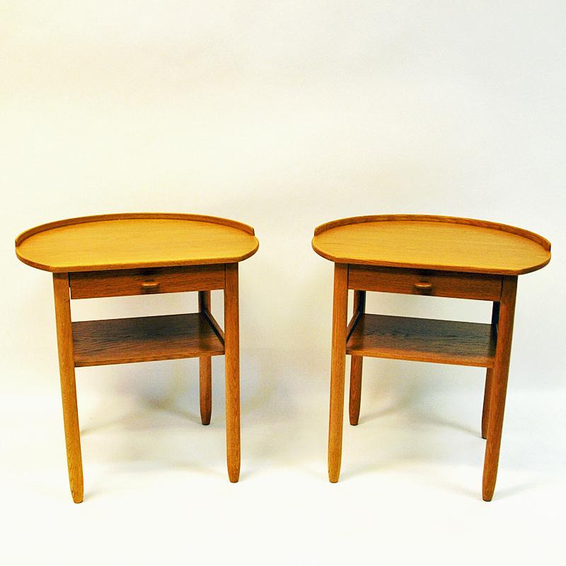 Pair of oak bedside/small tables by Sven Engström and Gunnar Myrstrand for Bodafors in 1964. Beautiful rounded design on tabletops with a halfway edge or lip around them to prevent items from rolling off.
Sculpted drawer handles and a neat shelf