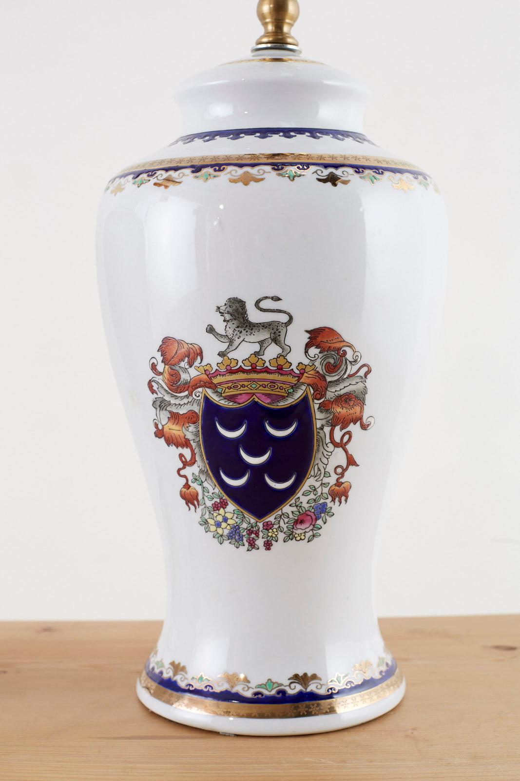 Stately pair of porcelain jar or vase table lamps featuring British style coat of arms motifs on each side. Each side depicts a royal shield in Lapis surmounted by a gold crown with a lion on top. Beautifully decorated with gilt highlights and