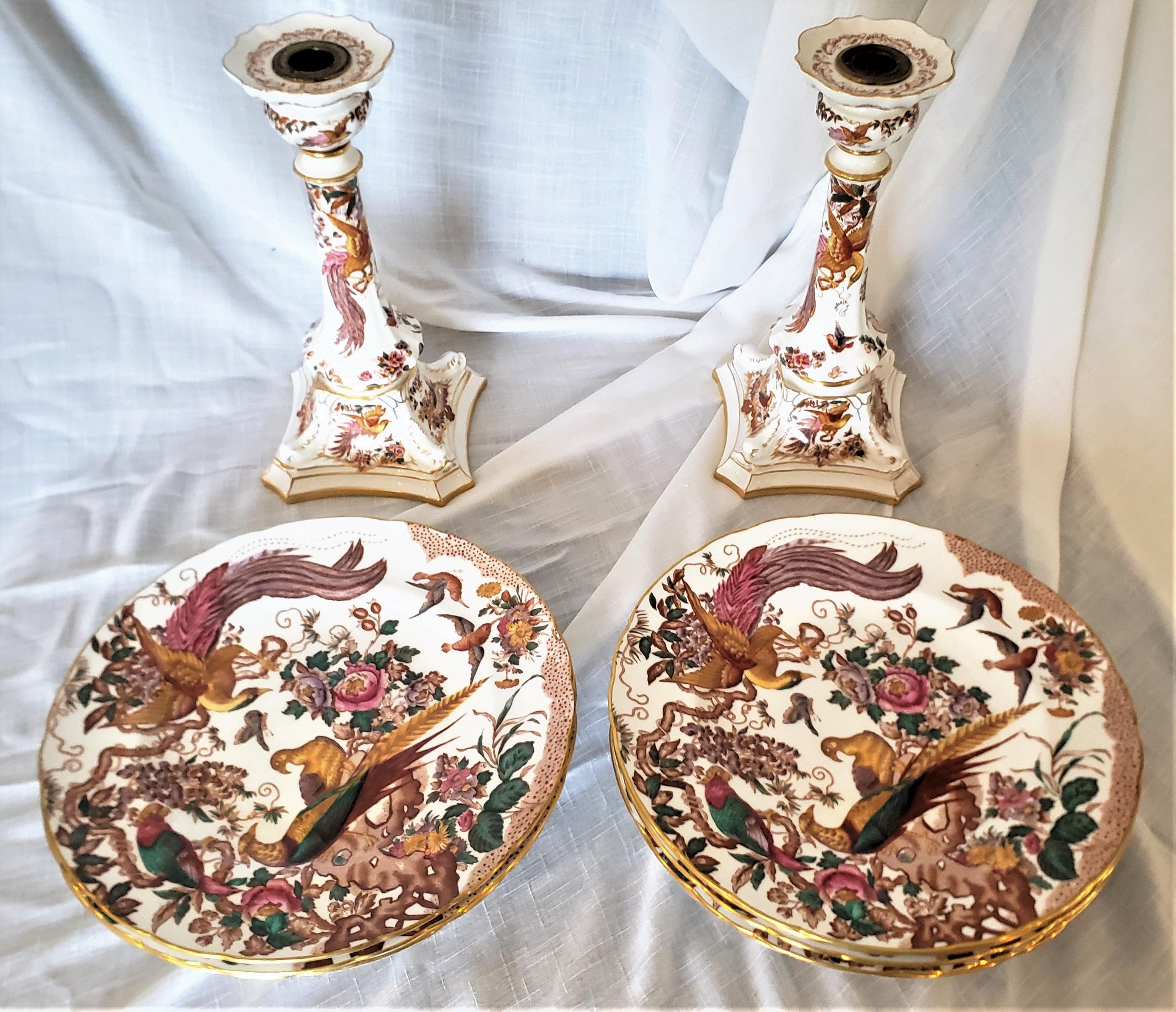 These tall candlesticks and dinner plates were made by the renowned English porcelain maker, Royal Crown Derby. The candlesticks and plates are done in their 'Olde Avesbury' pattern with vibrant exotic birds as decoration. The backstamps date to