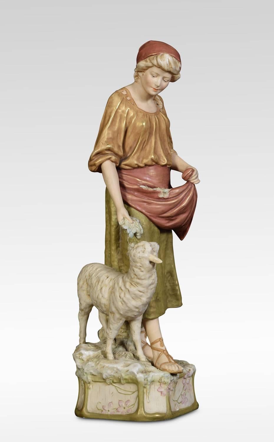 Ein Paar Royal Dux Bohemia Porzellanfiguren eines Ziegenhirten in Tierfell mit einer Ziege am Fuß und einer Hirtin, die ein Mutterschaf am Fuß mit Futter aus ihrer Schürze füttert, beide auf gekanteten quadratischen Sockeln, beide mit rosa