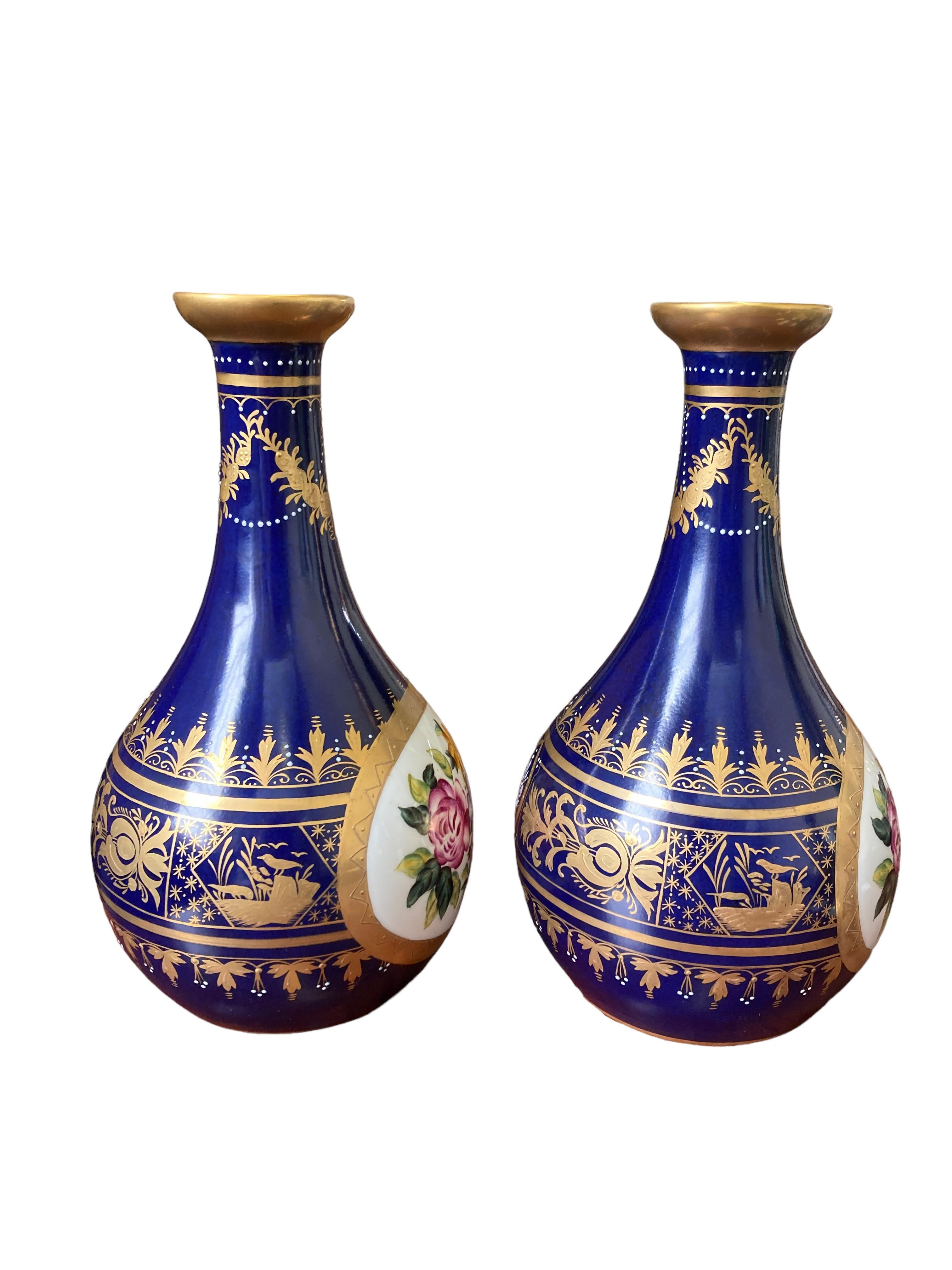 This beautiful pair of Royal Vienna bud vases is in excellent condition, with no damage to either vase. There is a small area at one of the top rims of a circular spot in the gold paint, as shown in a photo, which is original to when the pieces were