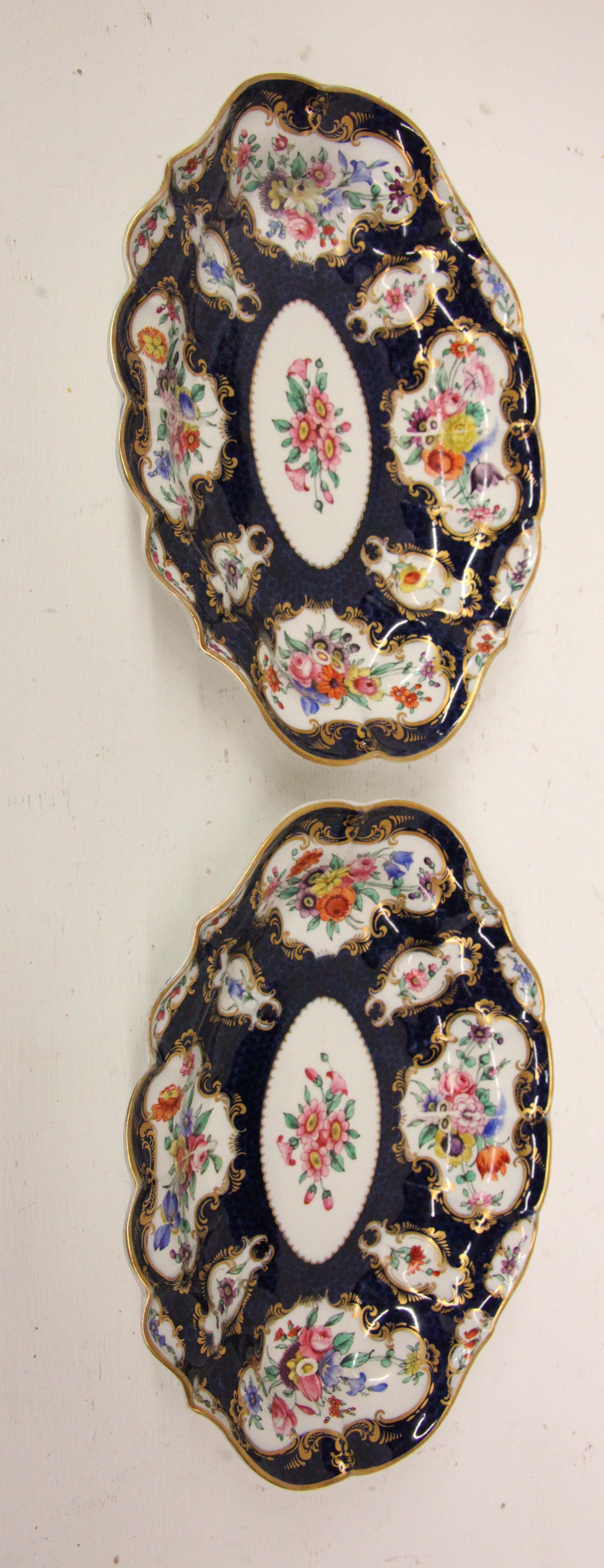 Paire de plats ovales Royal Worcester, magnifiquement façonnés avec la bordure remplie de panneaux floraux sur un fond cobalt, rehaussé de dorures sur toute la surface, le centre ovale avec un bouquet de fleurs.