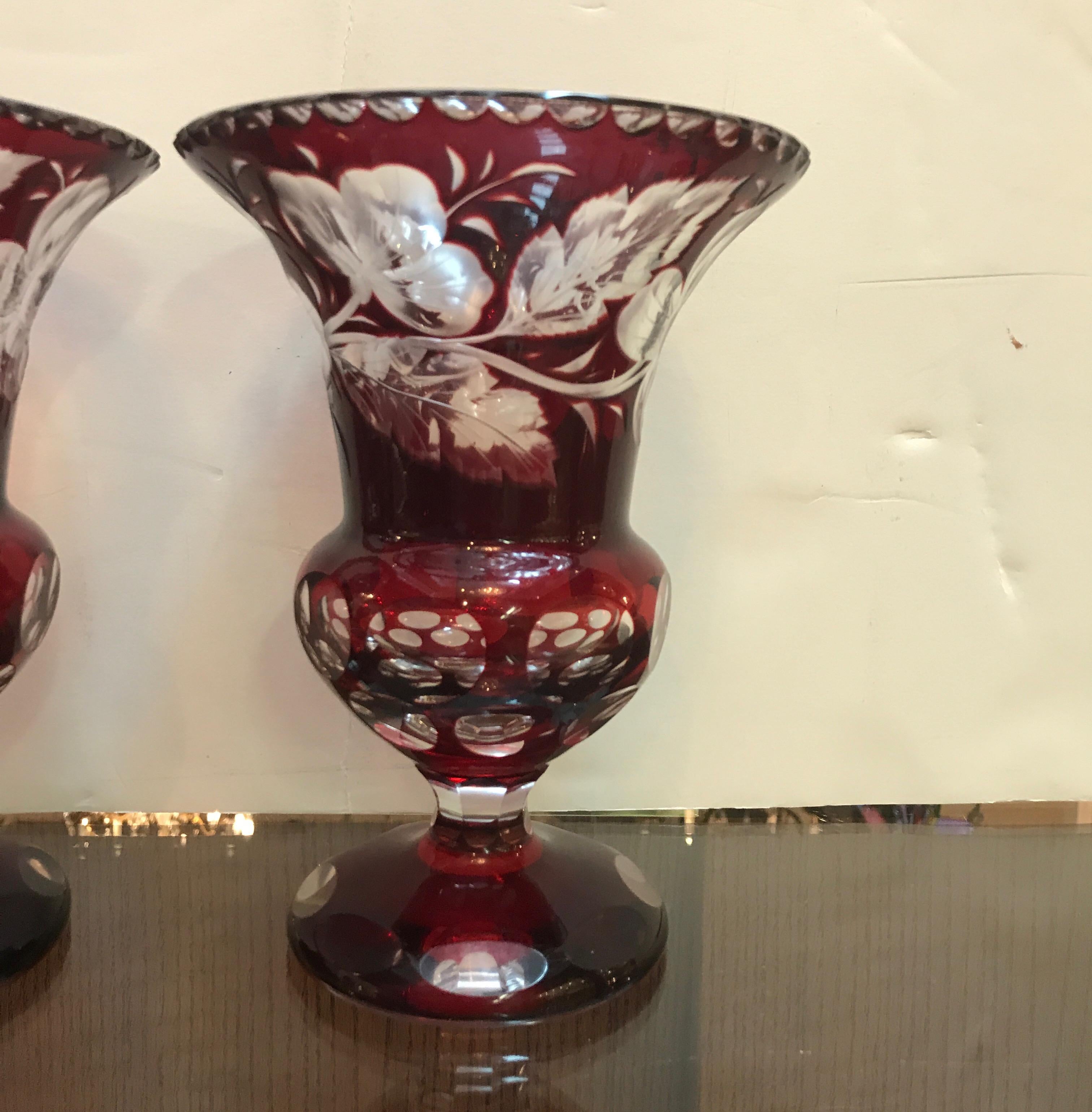 A pair of intaglio cut-glass ruby cased over clear. The Campana urn form with cased ruby glass intaglio cut to reveal the clear base. Elegant and formal with notched top edge, floral and leaf pattern on the main body with optic cut circles on the
