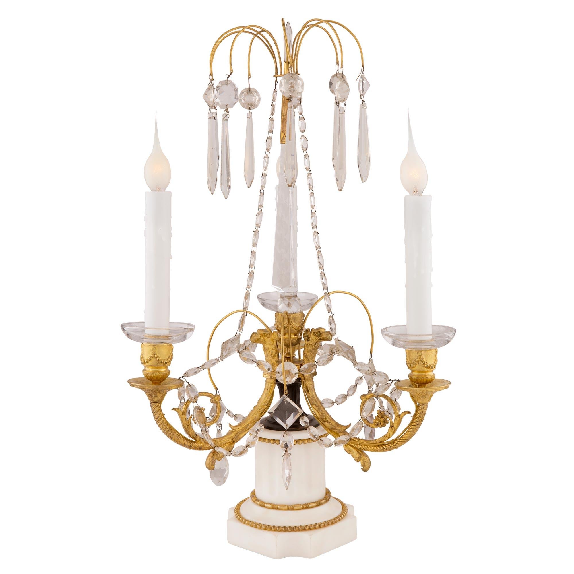 A most elegant pair of Russian early 19th century Neo-Classical st. ormolu, crystal and white Carrara marble three arm Girandole lamps. Each Girandole is raised by a square white Carrara marble base with concave corners, a mottled design and wrap