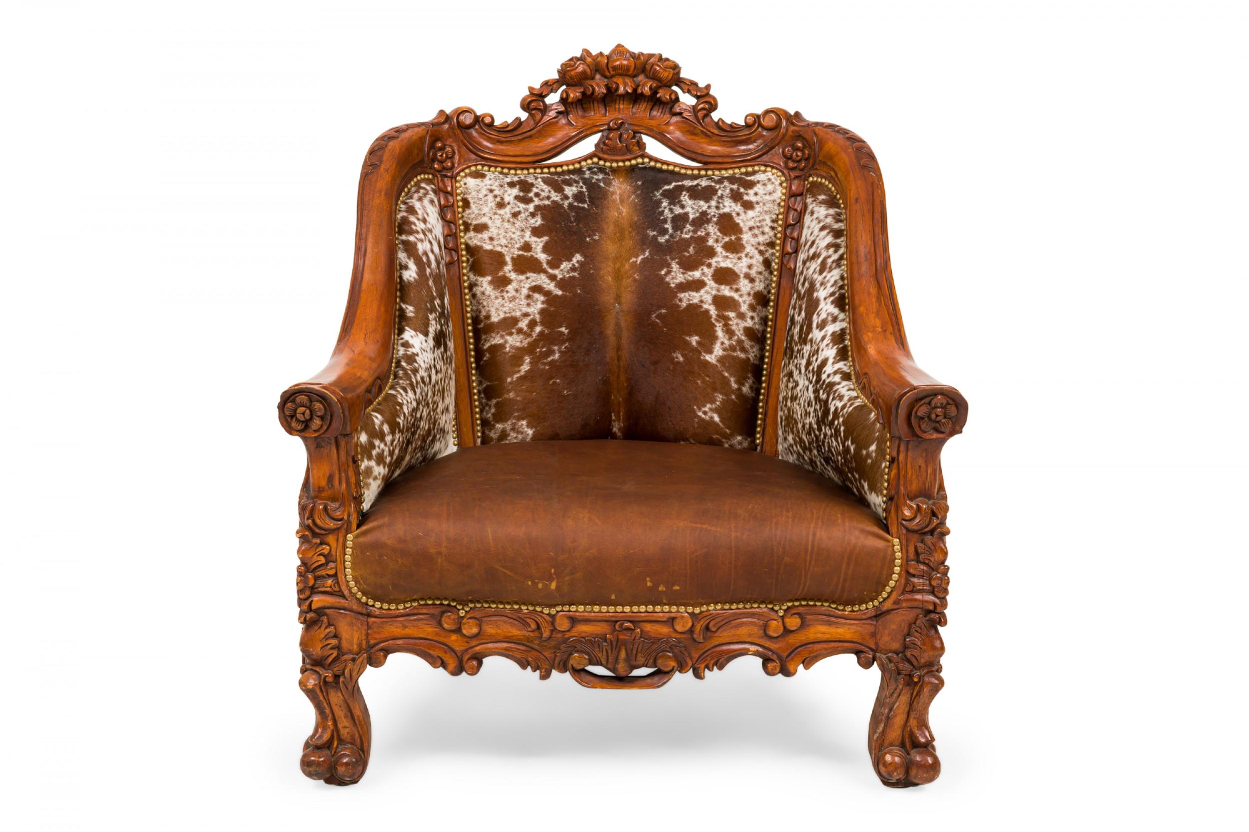 Pair of Rustic American custom arm / lounge chairs with carved walnut frames featuring a floral crest, with cowhide backs and sides and a brown leather upholstered seat with decorative nailhead trim, resting on carved paw feet. (priced as pair).