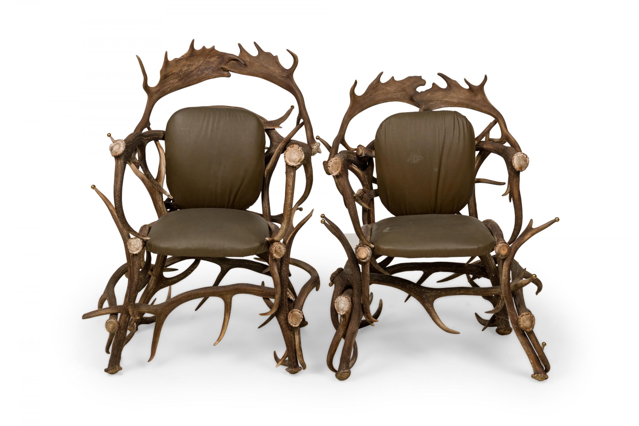 Pair of Rustic Continental-style armchairs with resin faux moose and deer antler constructed frame with points capped with decorative brass balls, and dark olive green upholstered seats and backs. (Priced as pair).