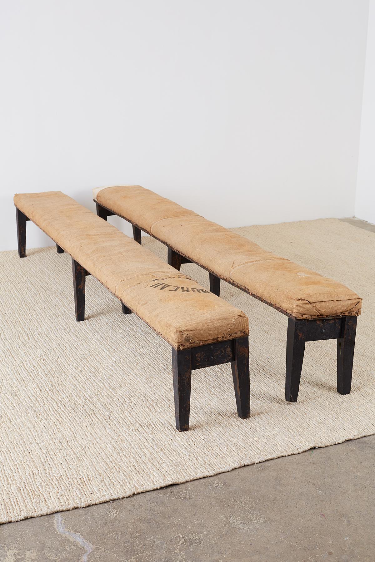 Sensational pair of long rustic French farmhouse benches from the early 20th century. Beautiful distressed patina upholstered in an antique burlap fabric with nail head trim. Each bench is supported by six tapered wood legs with iron straps. One