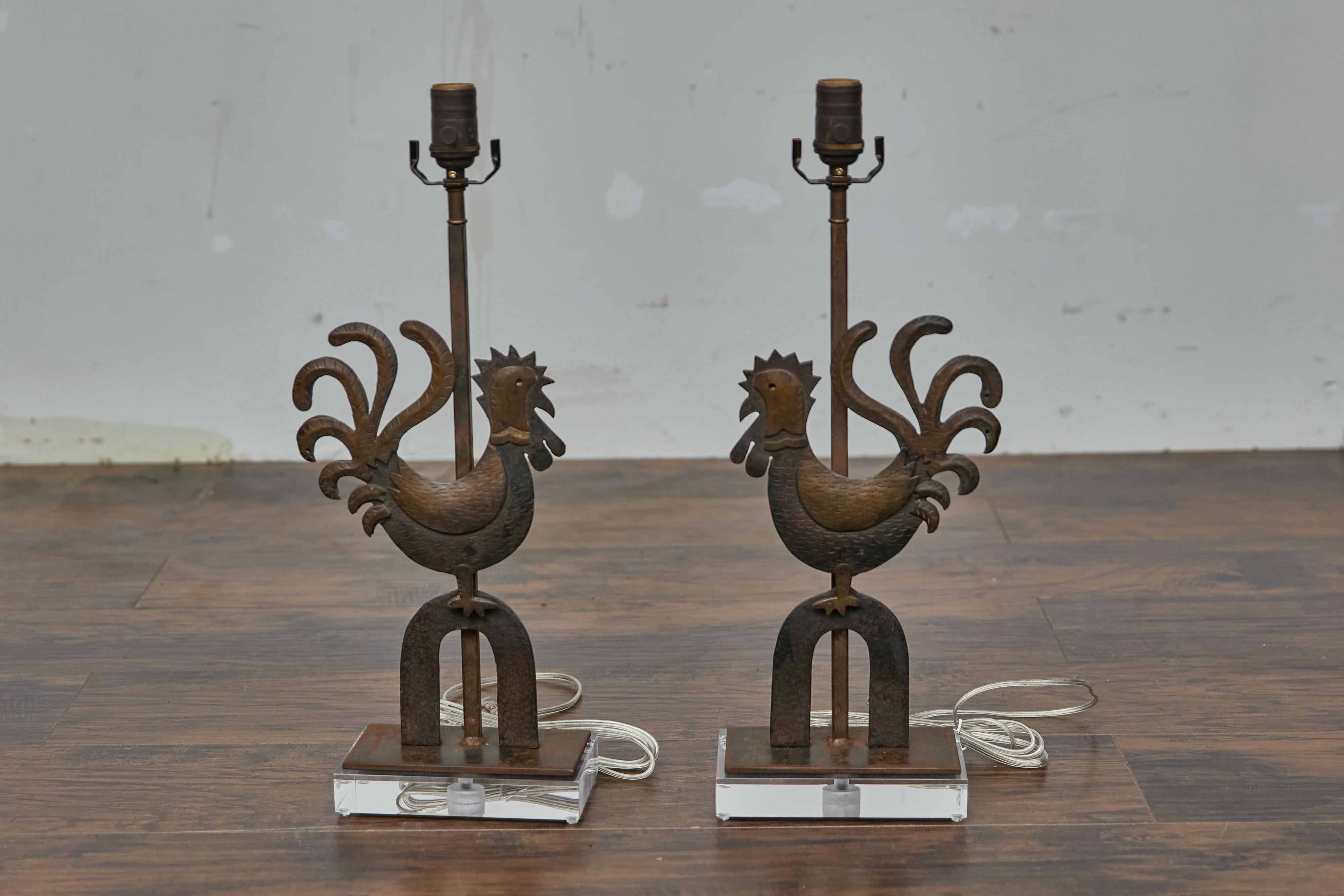 A pair of French Turn of the Century wrought iron roosters made into table lamps with Lucite bases. This pair of rustic French wrought iron rooster sculptures, dating to circa 1900, has been thoughtfully transformed into modern table lamps. Each