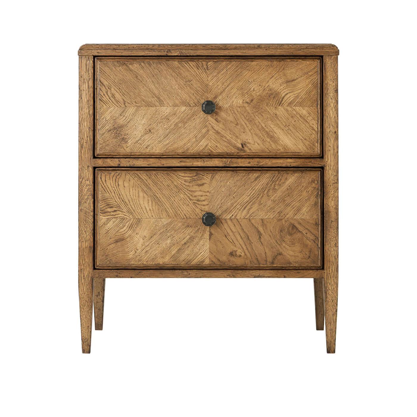 A rustic light oak two-drawer nightstand with a herringbone parquetry design. This beautiful nightstand has two frieze-inspired drawers with Verde Bronze handles. It is supported by two-tier stretcher shelves. 

Shown in Dawn Finish
Dimensions: