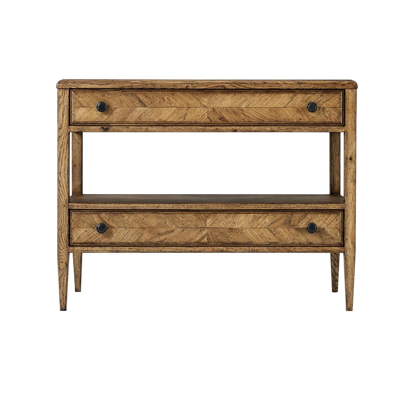Crafted with a striking herringbone parquetry pattern across its surfaces, this piece features two drawers for discreet storage. Each drawer is adorned with Verde Bronze finished handles, offering a subtle contrast to the warmth of the oak. Tapered