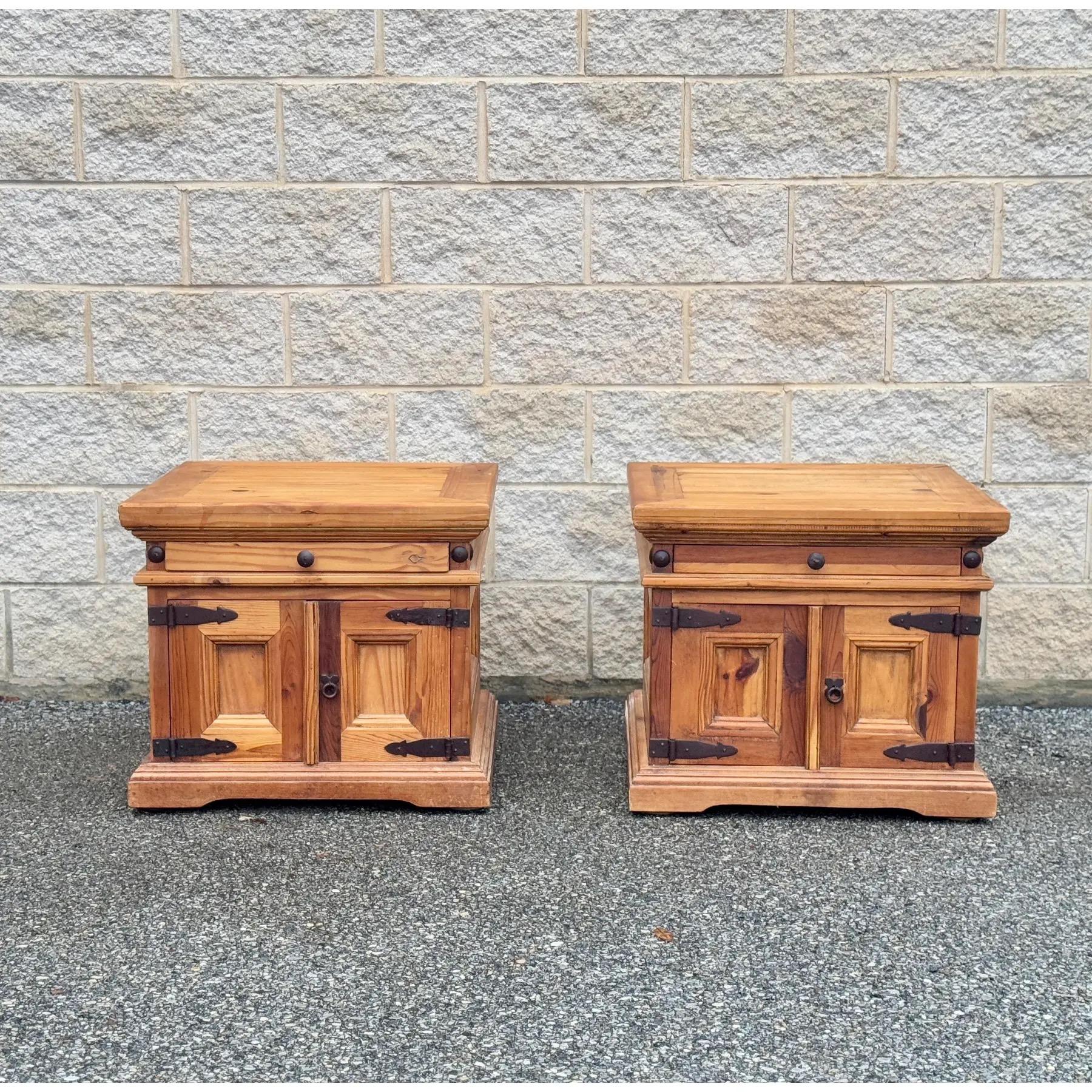 A pair of solid pine nightstands made in Mexico. Featuring warm wood tones, sturdy construction, and wrought iron hardware, these pieces offer classic rustic style and functional storage with a drawer and double-door cabinet. 