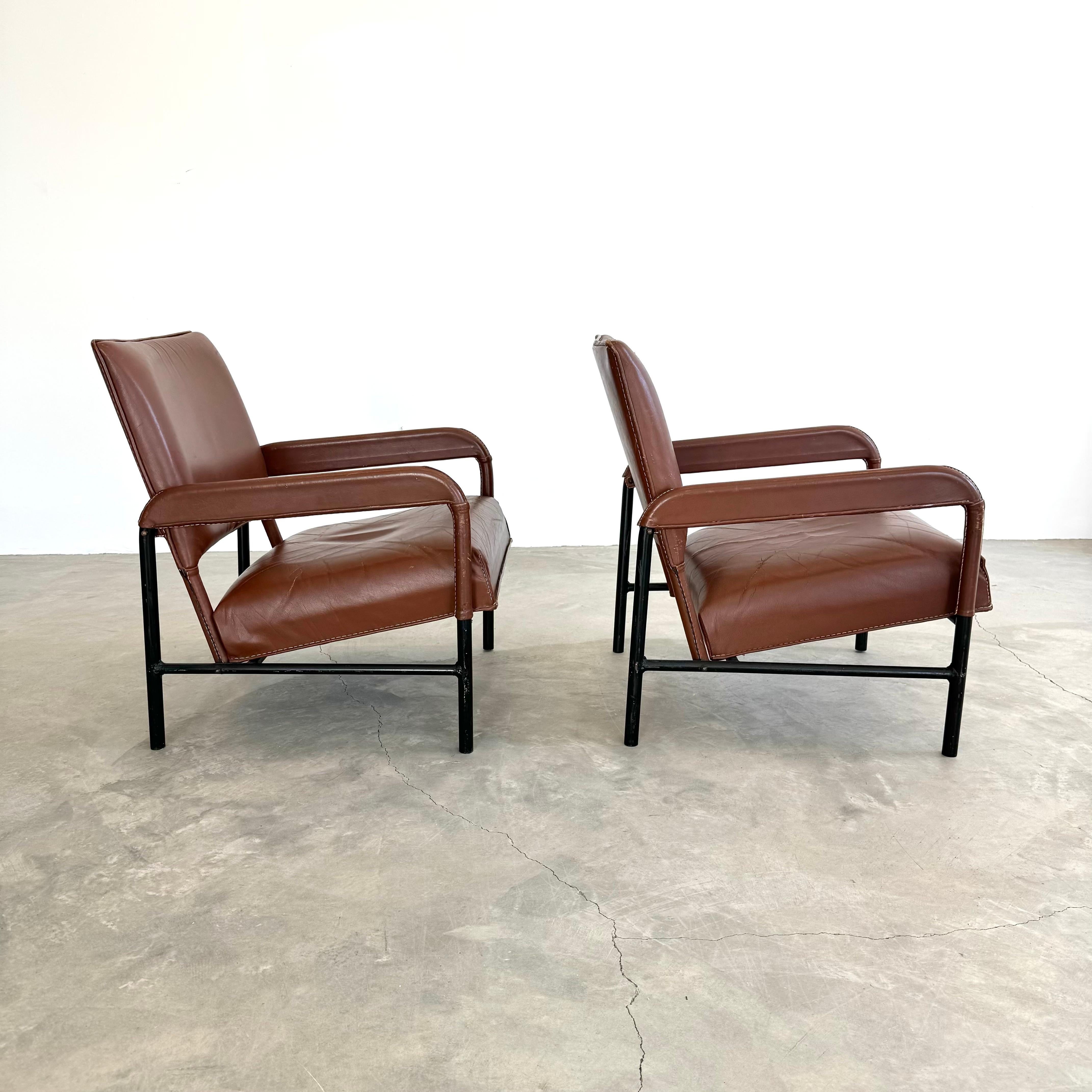 Important pair of armchairs by French designer Jacques Adnet. Heavy, tubular iron frame makes a substantial and grounded seat. Cognac saddle leather with signature Adnet contrast stitching. Thick leather seat bottom and plush leather seat back.