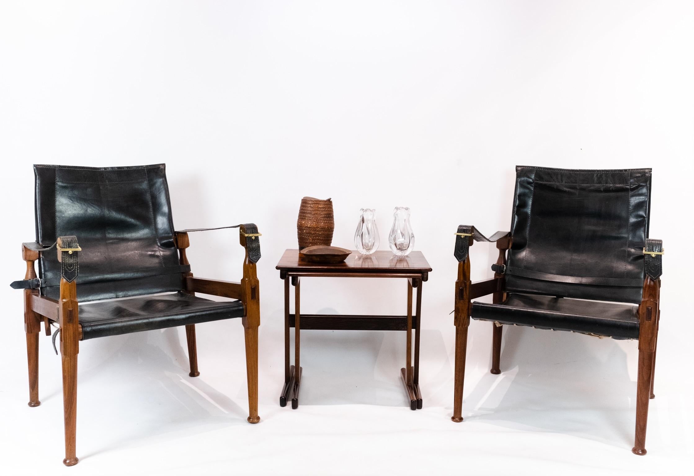 A pair of Safari chairs in walnut and black patinated leather from the circa 1960s is a stylish and classic addition to any interior space.

Safari chairs, also known as campaign chairs, are known for their portable and collapsible design, making