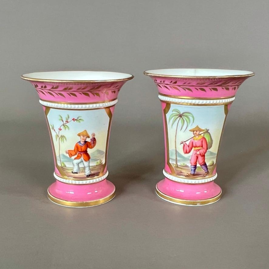 An extremely rare pair of small porcelain spill vases with a white pearled ring around the body, a bright pink ground and beautiful octagonal reserves with charming Chinoiserie paintings, one of a traveller with a knapsack by a palm tree, the other