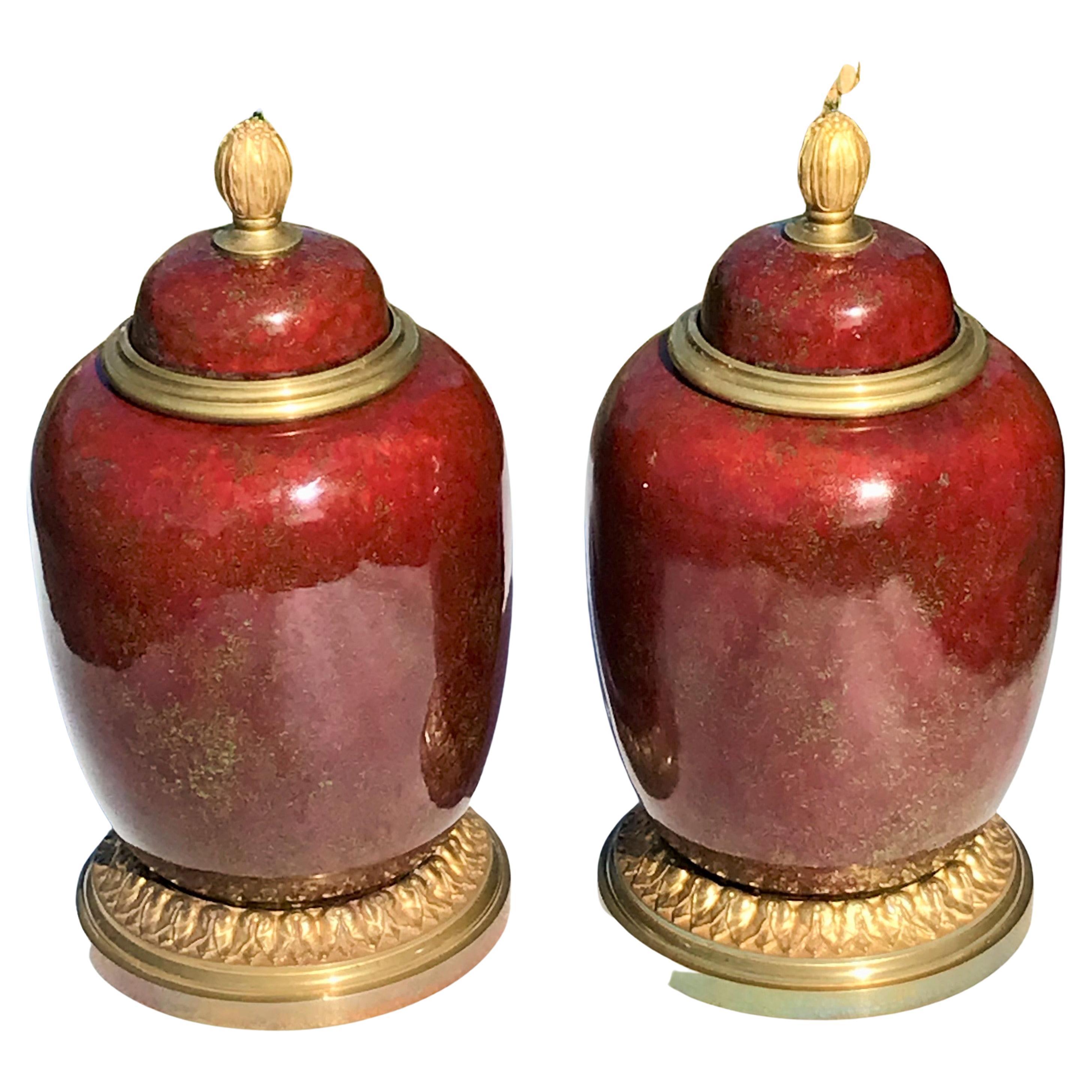 A gilt bronze mounted pair of flambé' porcelain jars or urns. The oxblood color with flecks of gold and chartreuse. In brighter lighting the the color becomes a brilliant ruby. Both present very well. Can be used with or without the bronze lid