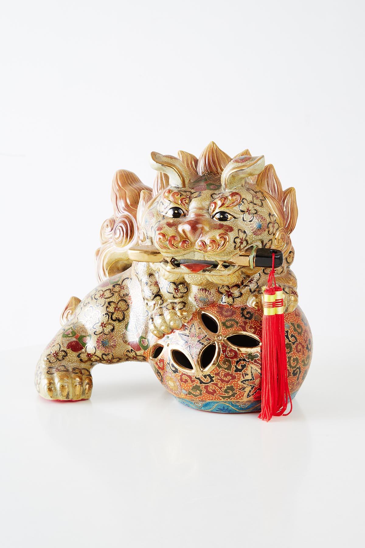 Pair of satsuma style gilt porcelain style foo lions. Each lion having a dagger in its jaw and paws on a ball with red tassels. Beautiful hand-painted details in golds, reds, browns and cream.