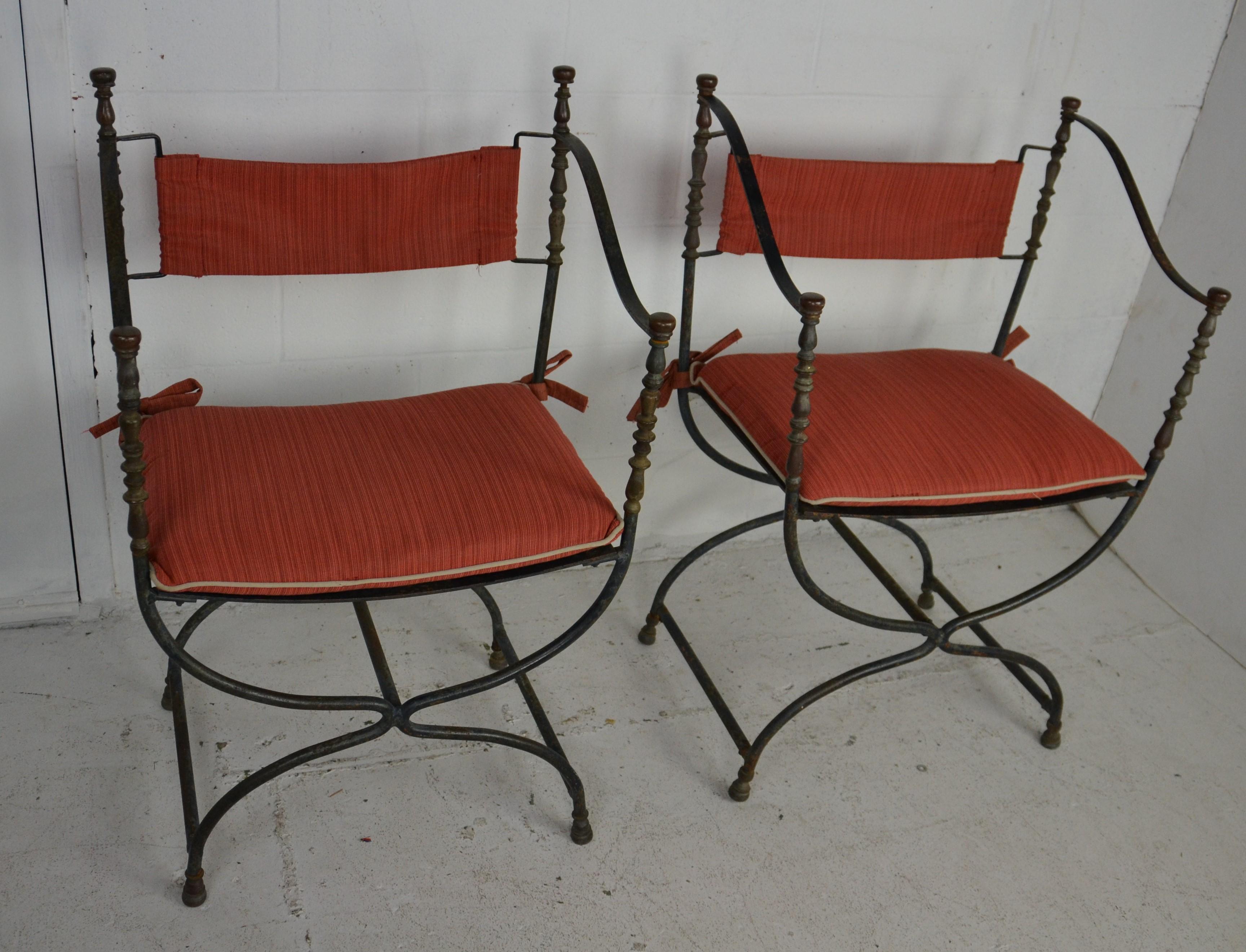 A pair of Italian Savonarola iron and brass chairs in a Campaign style. Iron frames with turned brass upper supports and finials. Old patina. Slight variation in arms. Arms reach to the top of the back frame on one chair and a little lower on the