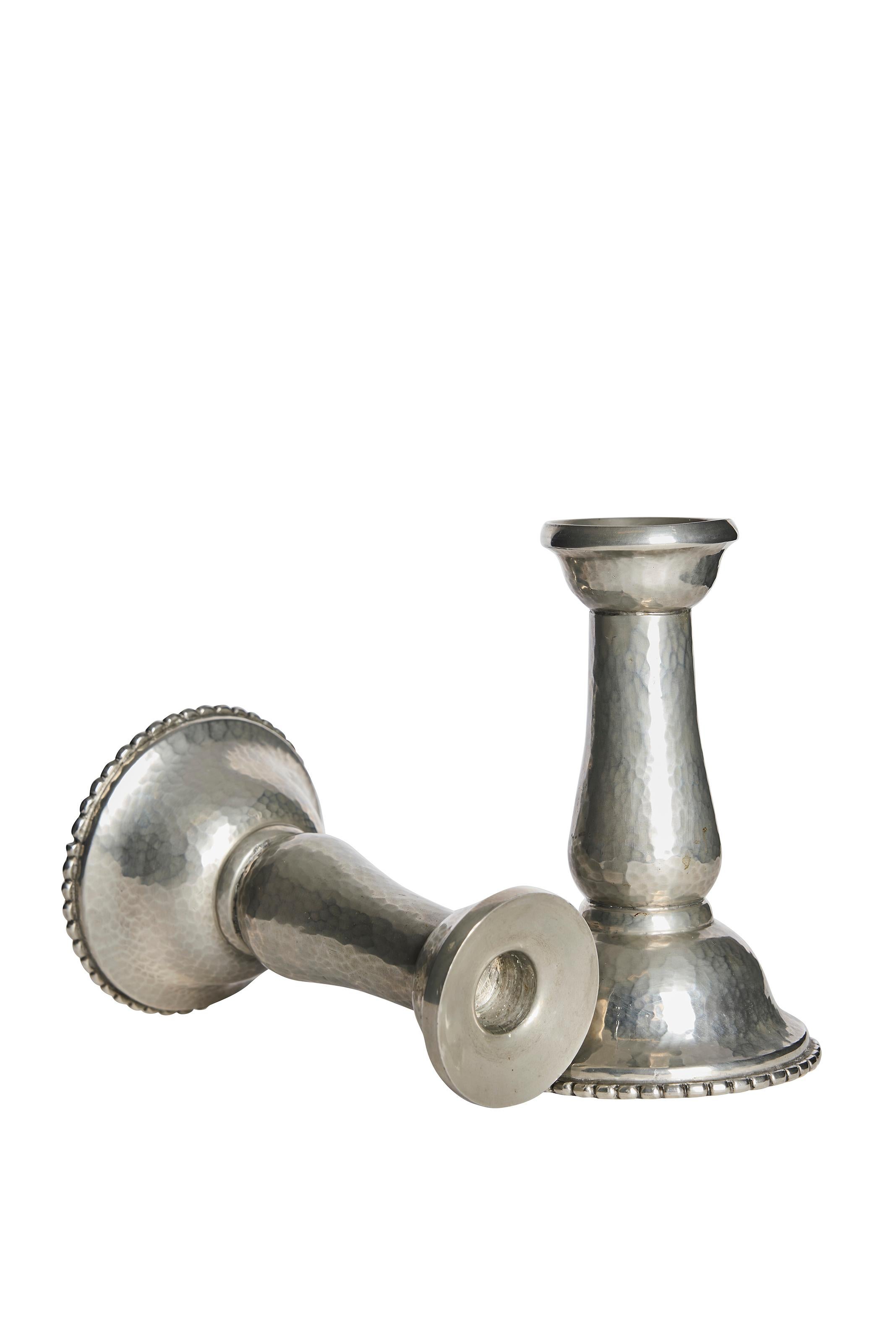 Realizzata in Danimarca negli anni '30, questa elegante coppia di candelieri in peltro martellato a mano di Kunst Tinn riflette la raffinata abilità artigianale e lo stile decorativo delle arti decorative scandinave. Con le loro silhouette