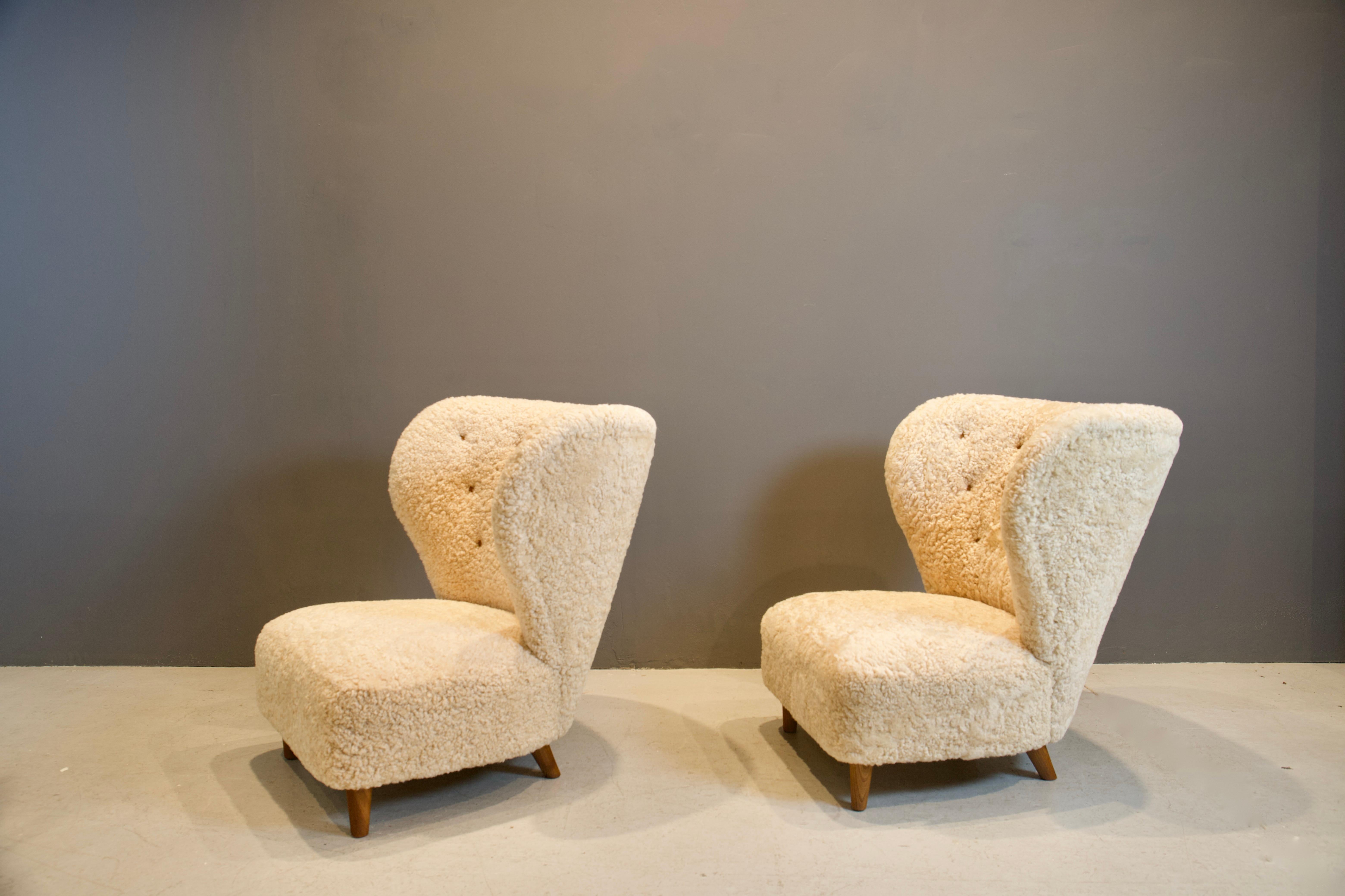 Sculptural pair of Scandinavian low chairs, newly upholstered in light beige shearling hides, with brown leather button details. Round tapered oak legs.
Beautiful form and luxurious comfort.

These chairs are available to view in my NY gallery.