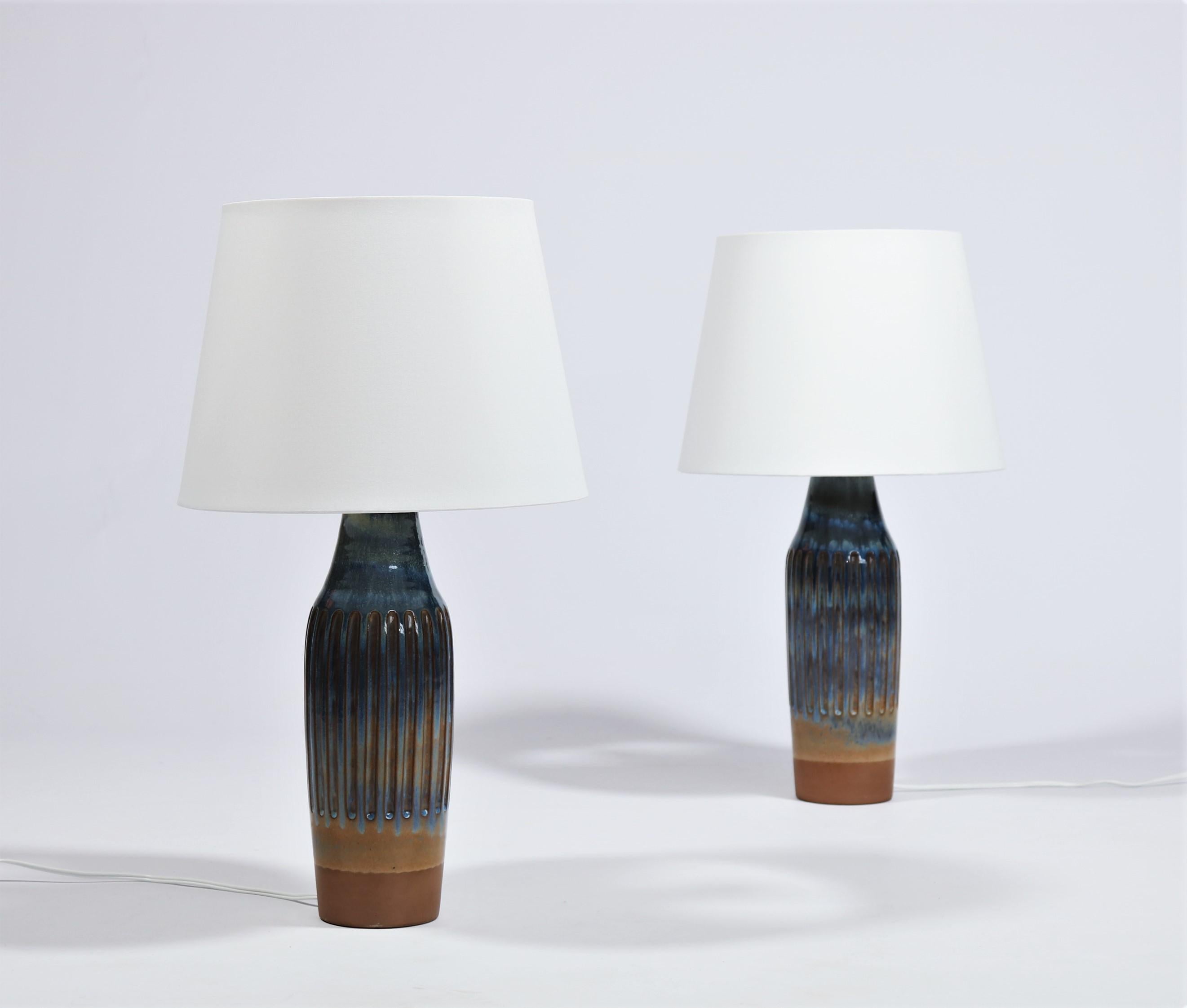 Stunning pair of ceramics table lamps model B 295 from 1964 made in Denmark in collaboration between ceramic workshop Michael Andersen & Son and lighting company Lyfa. Beautiful glossy blue nuanced glaze with notes of red, purple, turquoise and