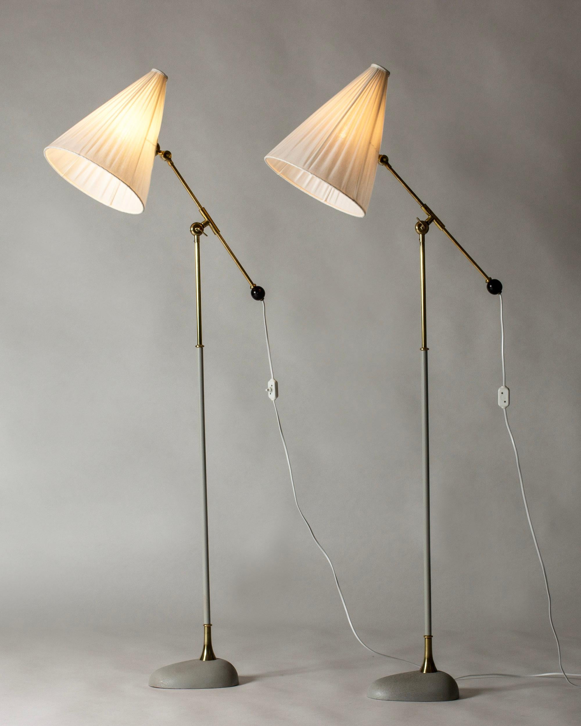 Pair of very cool floor lamps by Einar Bäckström, made from lacquered metal and brass. Chunky, oval bases lacquered light grey. Adjustable height and angle of the shades, cute ball shaped details, large pleated shades.