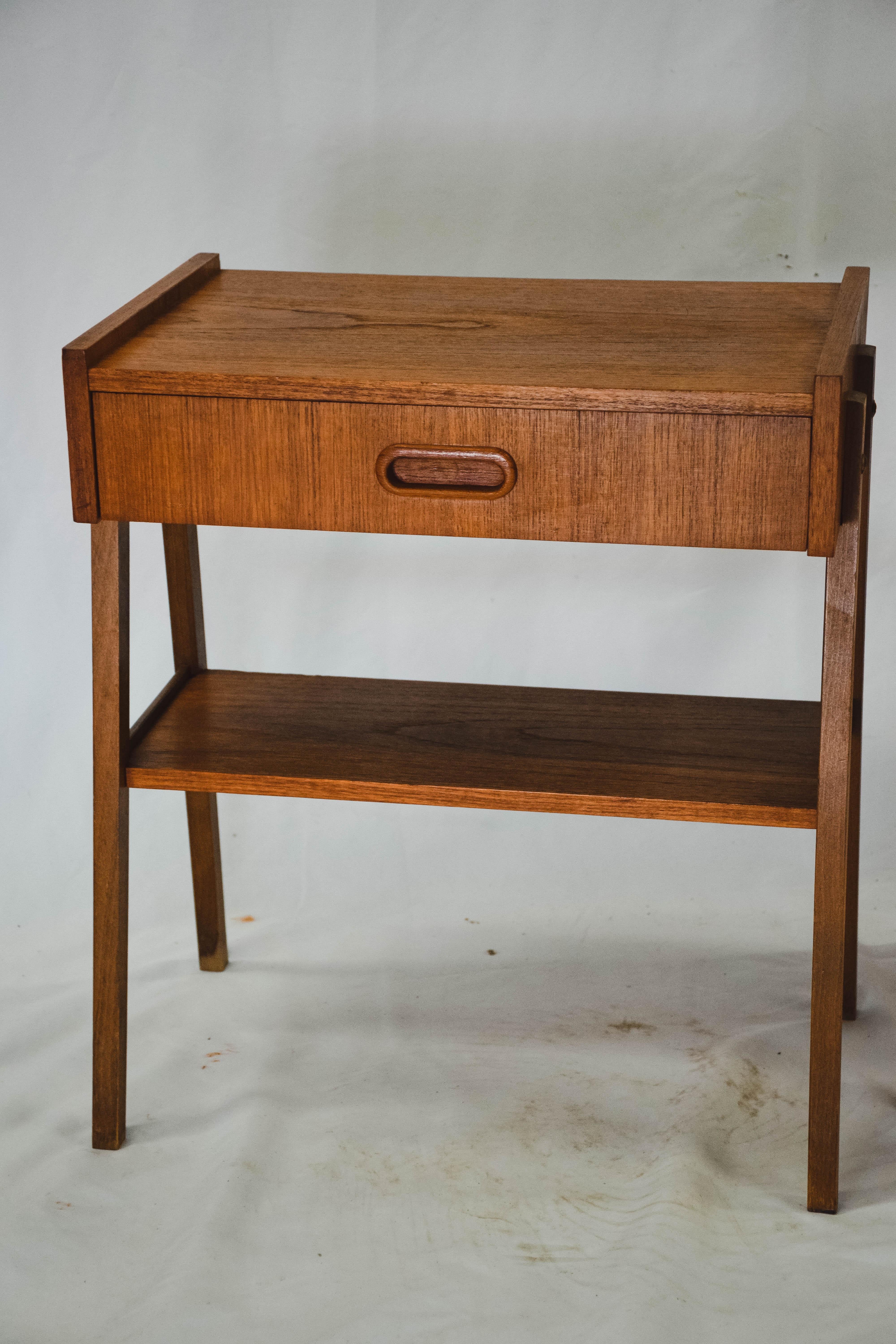 Lovely and elegant pair of vintage teak bedside tables with drawers and slightly outwards tilted front legs. These midcentury night tables have rounded legs and underneath a shelf for newspaper, books etc. Scandinavian design and good vintage