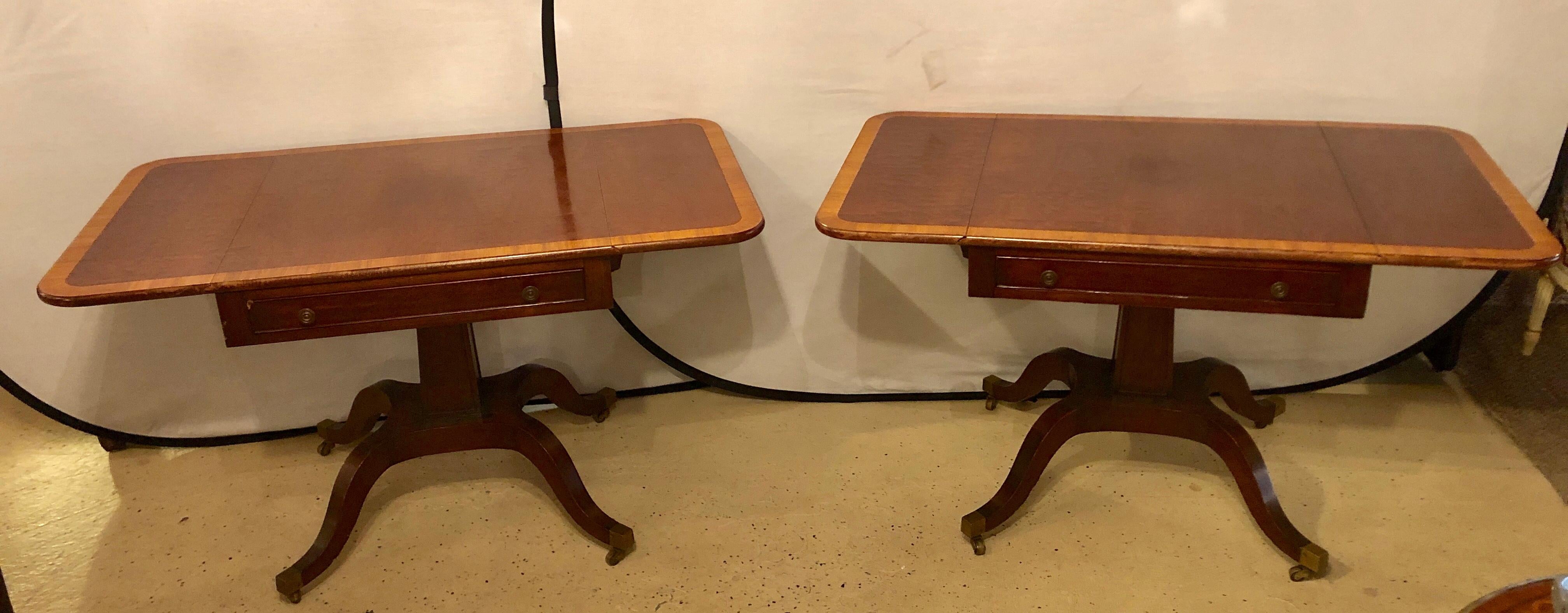 Pair of Schmieg & Kotzian Georgian style drop-leaf sofa or side tables. A fine pair of mahogany top with a satinwood banding along the edges having a single drawer leading to a pedestal quad legged base terminating in bass sabots with casters. These