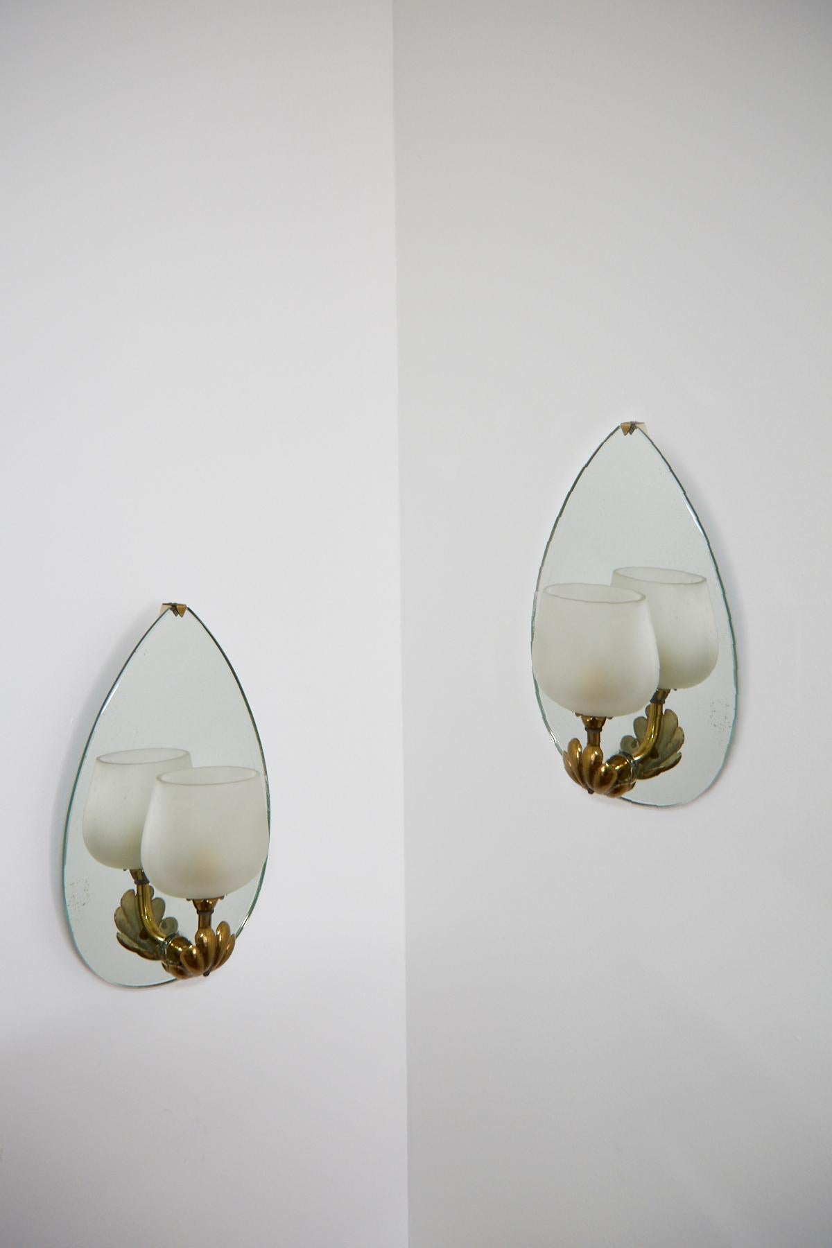 Elegant vintage pair of mirror-backed sconces in tear drop form, with a brass acanthus-covered arm supporting a frosted glass shade. Design by Pietro Chiesa and produced by Luigi Fontana. In working condition and hard-wired.