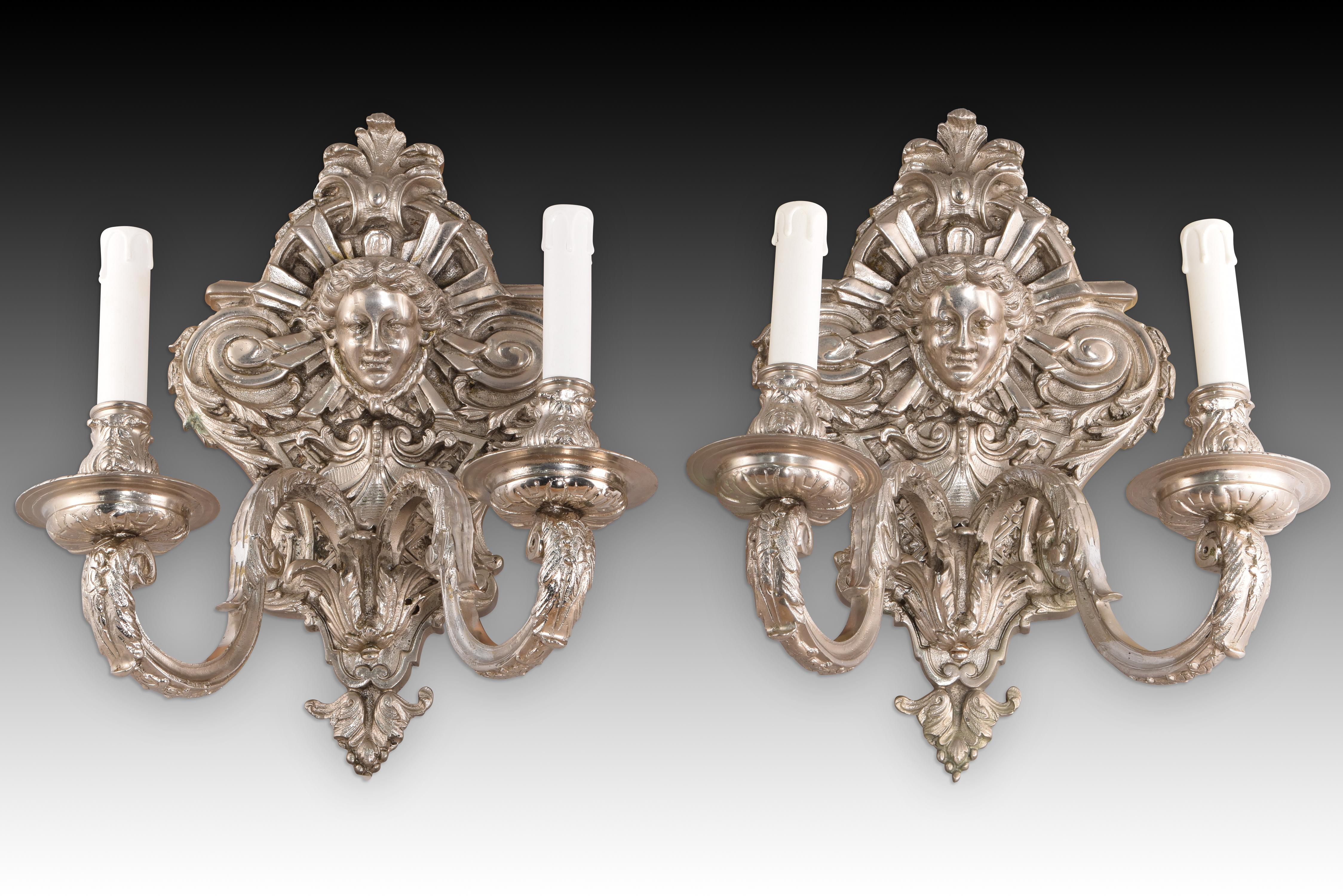 Coppia di appliques. Bronzo. Finitura argento.
Coppia di applique da parete a due luci ciascuna, decorate con motivi figurativi, vegetali e
decorato con elementi figurativi, vegetali e architettonici ispirati a certi rococò del XIX secolo.
Souvenir
