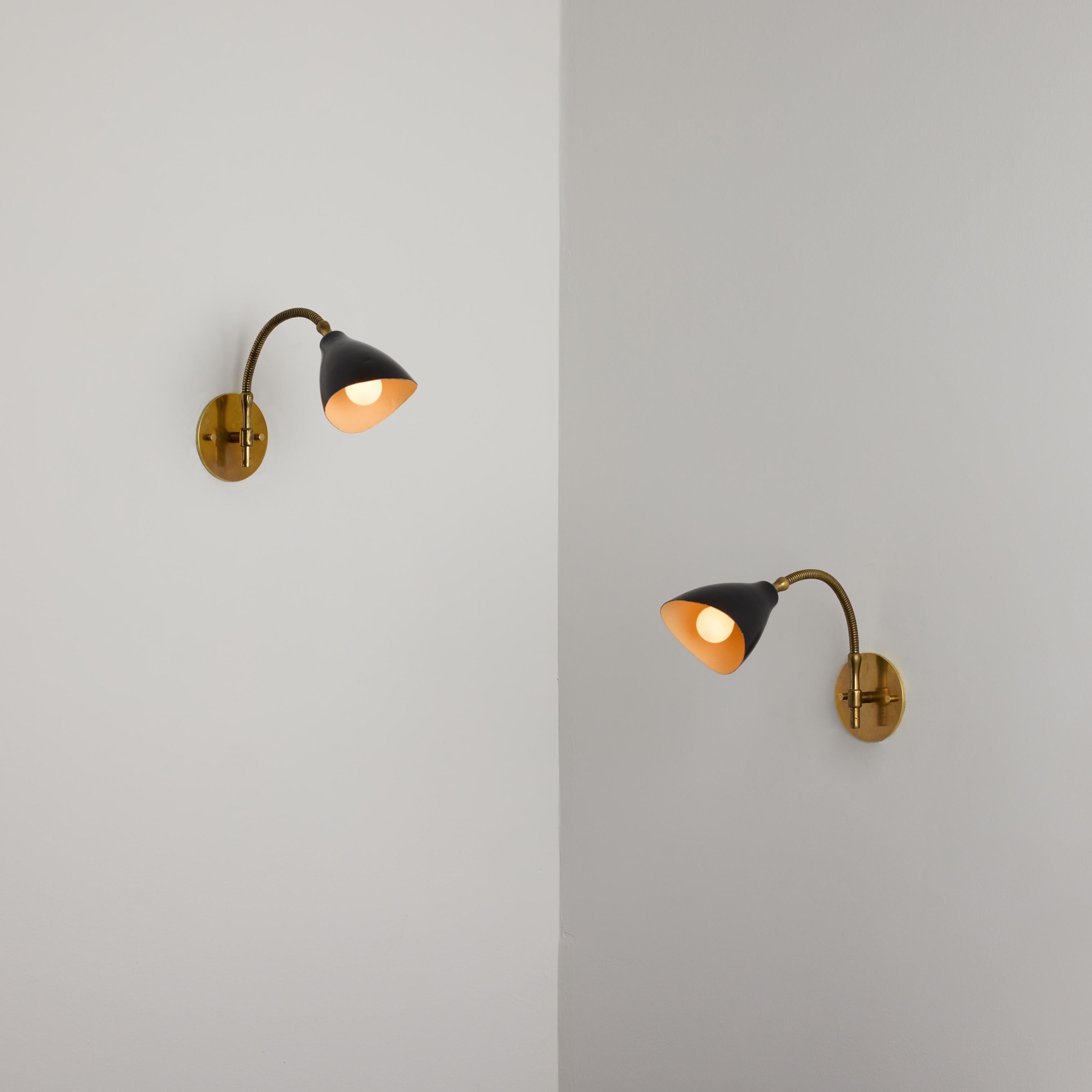 Paire d'appliques d'Angelo Lelii pour Arredoluce. Conçue et fabriquée en Italie vers les années 1950. Un abat-jour concave émaillé noir et une armature flexible en laiton composent ces étonnantes et délicates appliques. Chaque applique est équipée