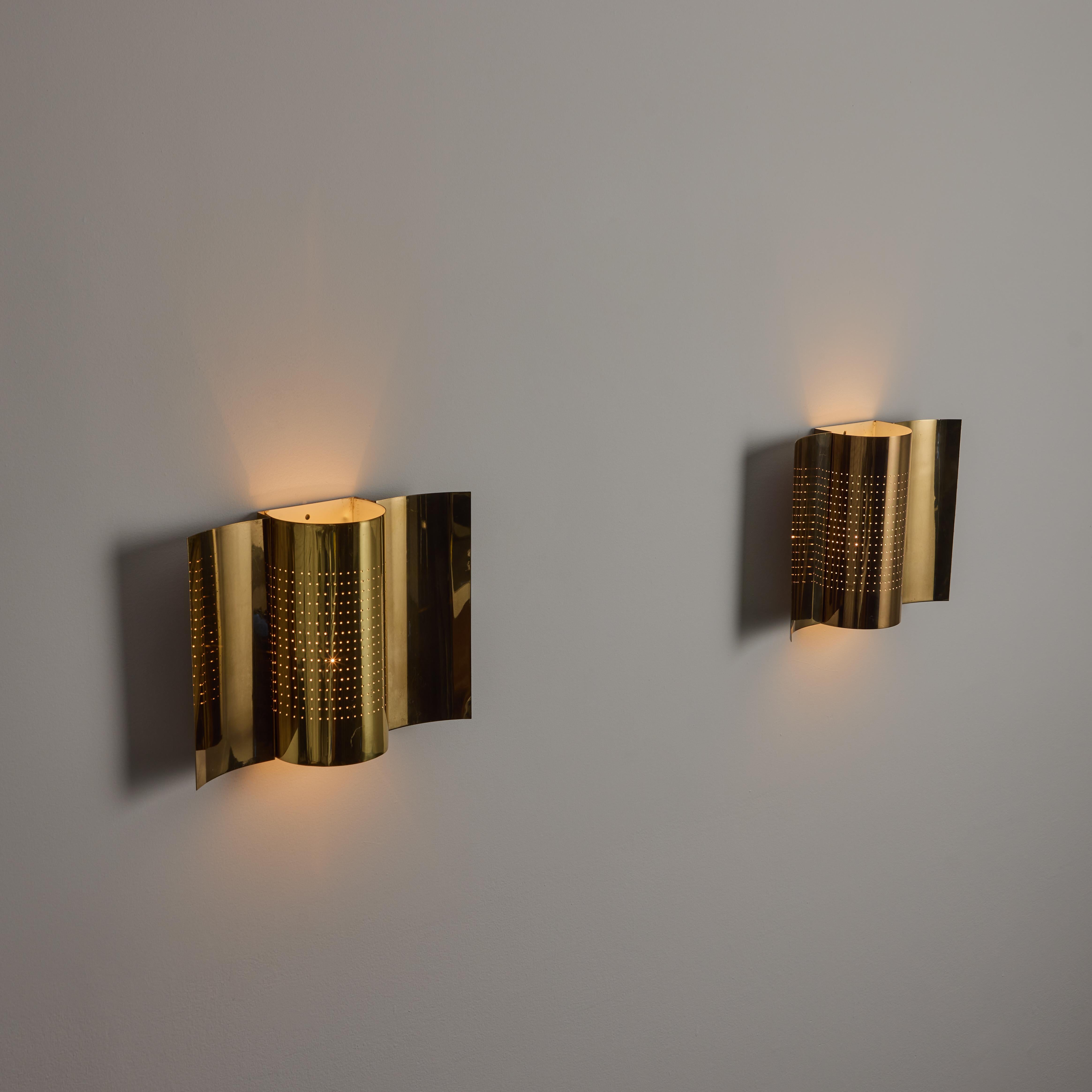 A Pair of Sconces by Haga Belysning. Designed and manufactured in Swedish, circa the 1970s. All polished brass shield sconces. A concave panel plate paired along with a perforated half cylinder. The lights hold a single E27 socket type, adapted for
