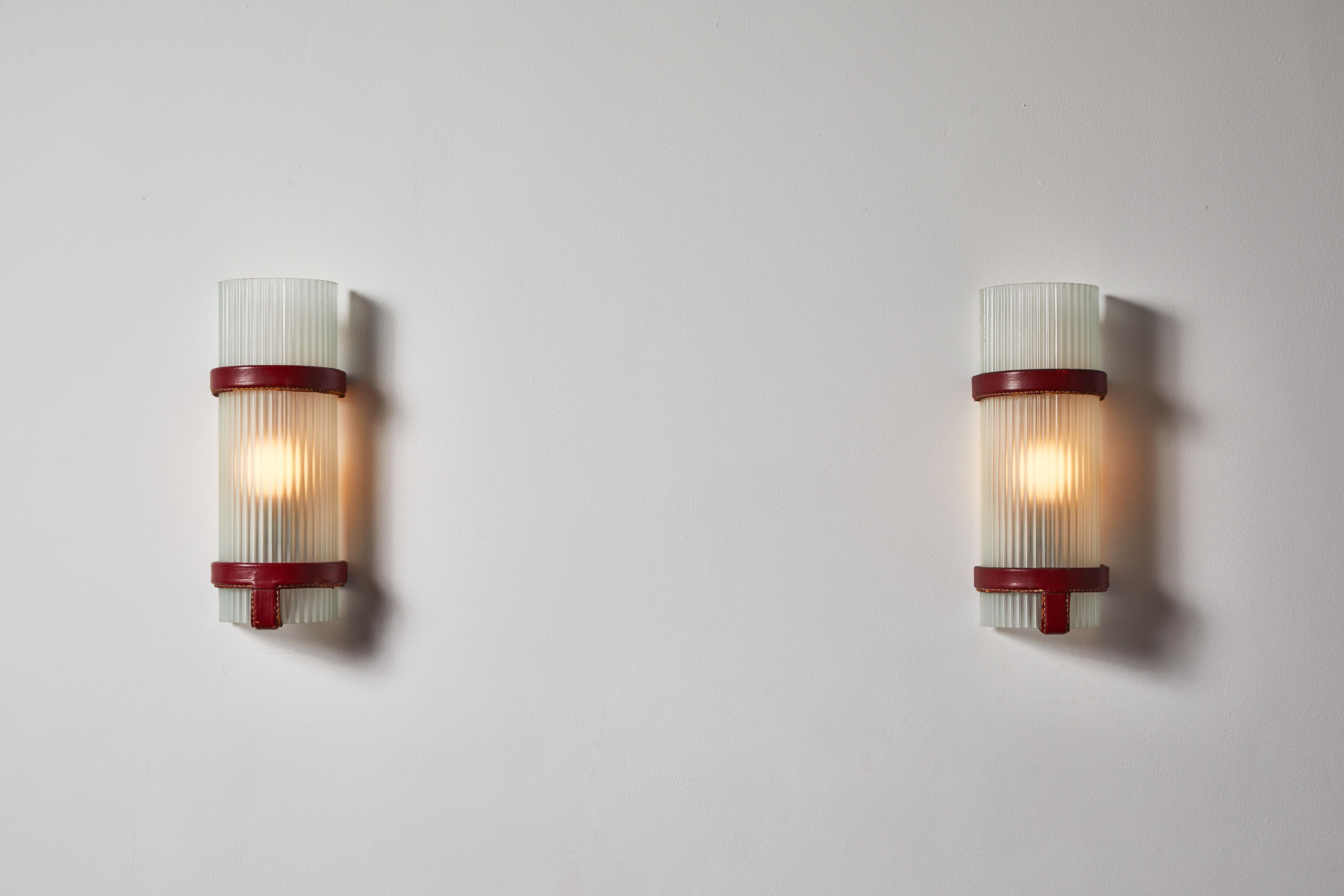 Pair of sconces by Jacques Adnet. Designed and manufactured in France, circa 1950s. Glass, with stitched leather. Rewired for U.S. junction boxes. Each light takes one E27 100w maximum bulb. Bulbs provided as a one time courtesy.
