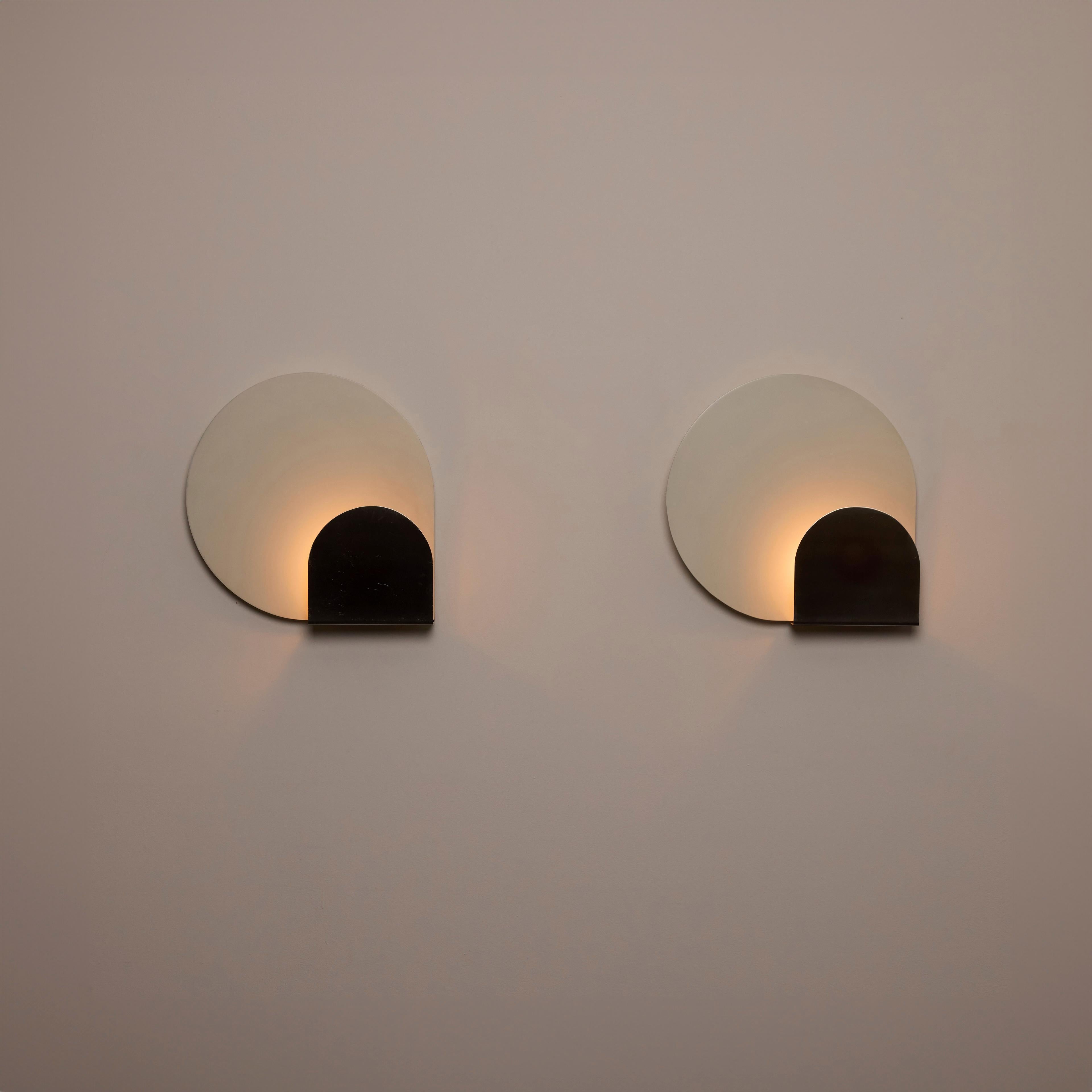 Coppia di lampade di Pia Guidetti Crippa per Lumi. Progettato e prodotto in Italia, intorno agli anni '1970. Applique geometriche in due parti che abbinano un retro smaltato bianco e un pezzo frontale in nichel spazzolato. L'acciaio anteriore è