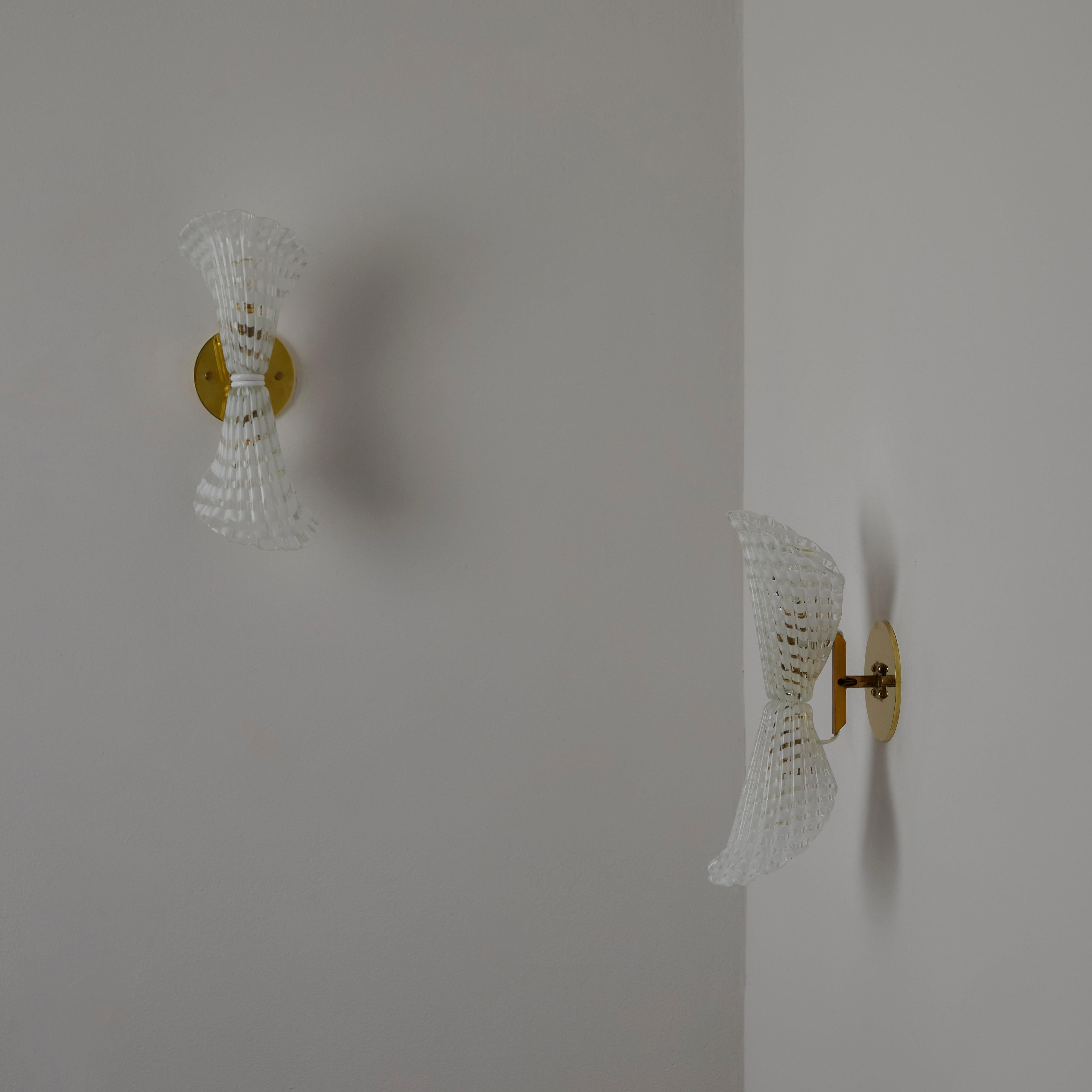 Pair of Sconces by Seguso. Designed and manufactured in Italy circa the 1950s. Gorgeous blown Murano glass sconces in the shape of trumpet flowers. The glass has an inlay of white cane. Each sconce holds two E14 socket-types, adapted for the US.
